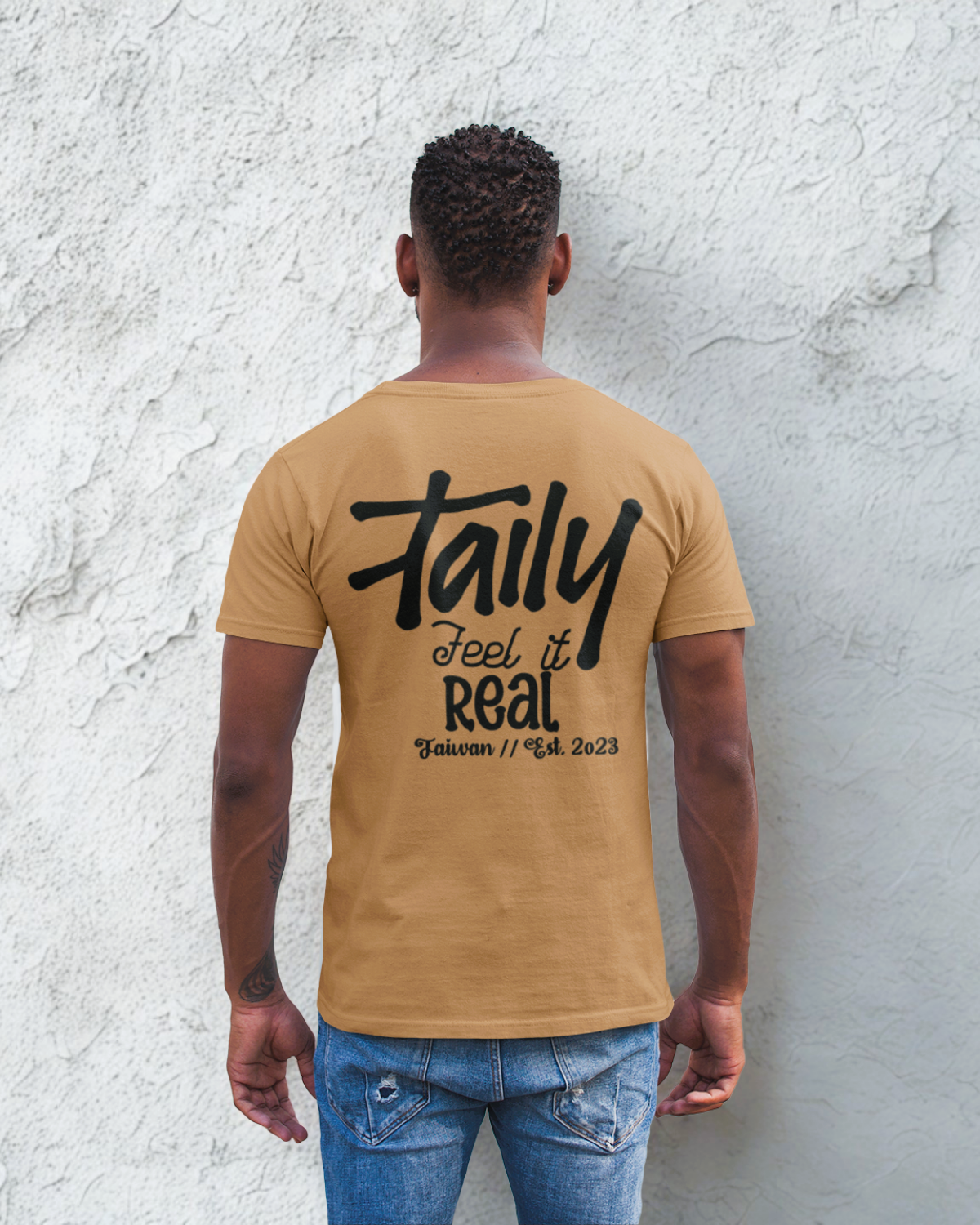 Back view of a man wearing Taily Feel It Real Boxy Tee in toast color with bold lettering.