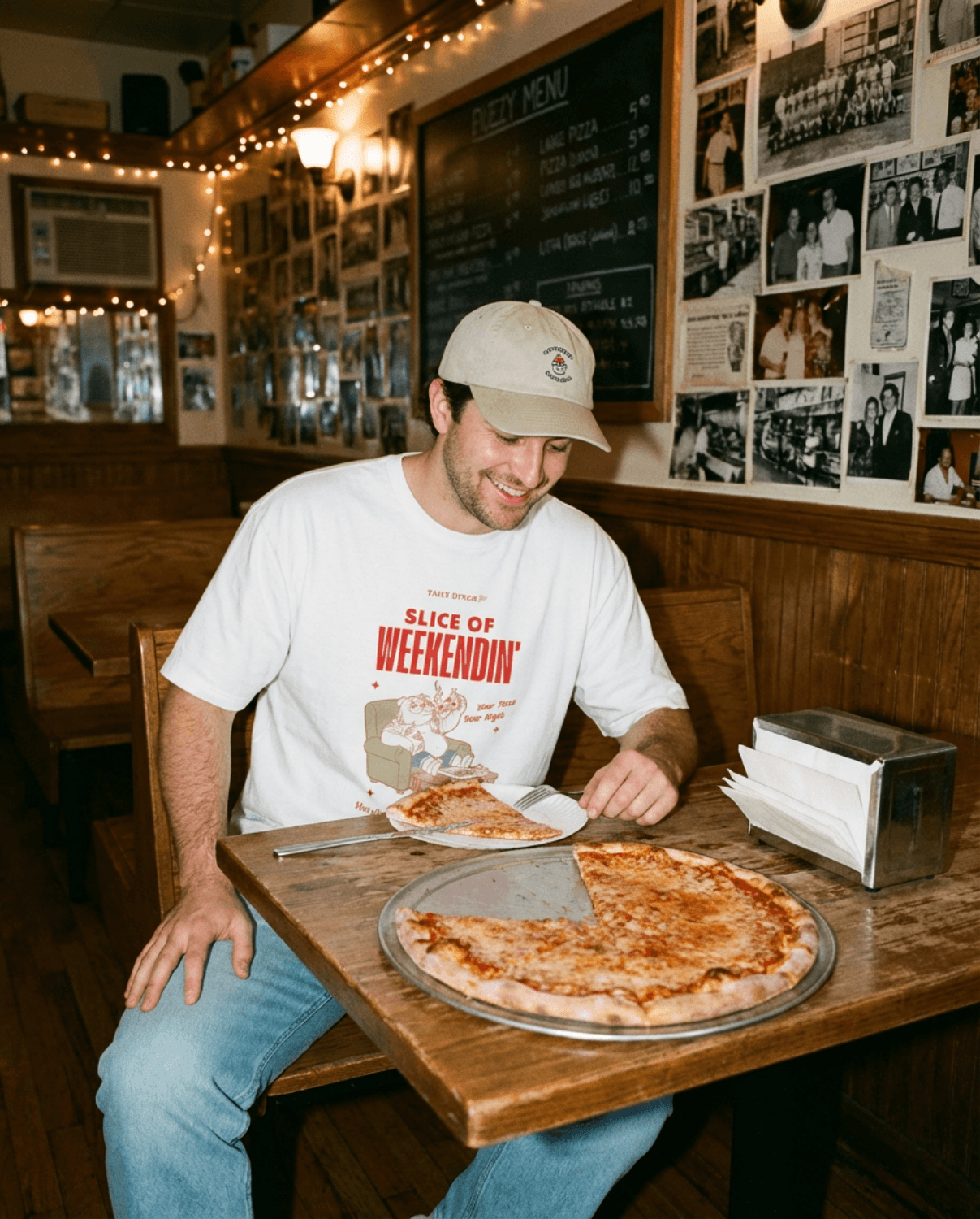Man enjoying pizza while wearing an Oversized Pizza T-Shirt – Slice of Weekendin’ (White) in a diner.