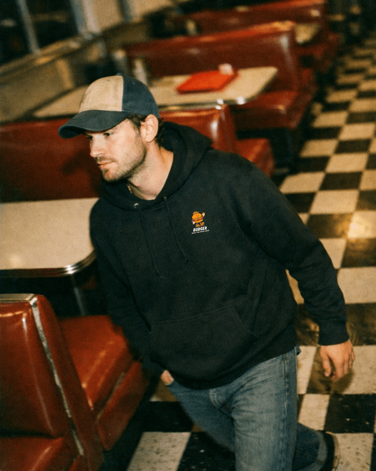 Man wearing Burger Hoodie – Good Times Service (Black) in a vintage diner setting.