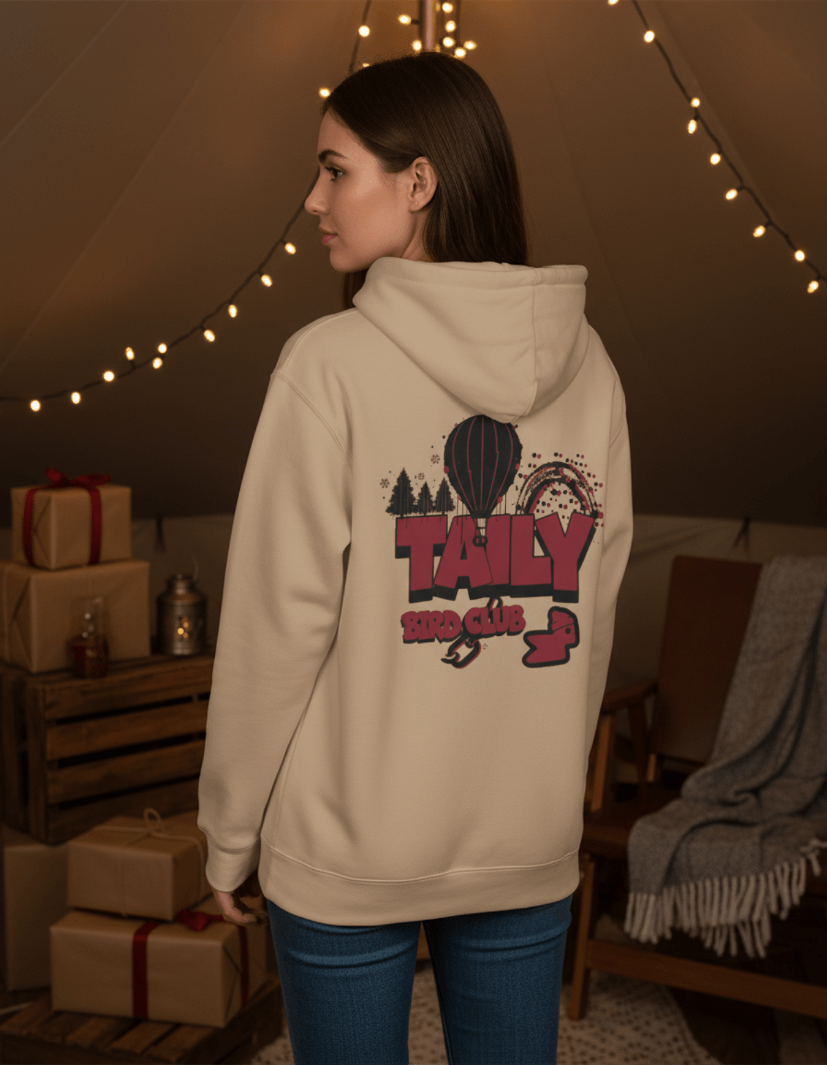 Taily Bird Parkland Hoodie – Sandstone with graphic design, worn by woman in cozy setting.