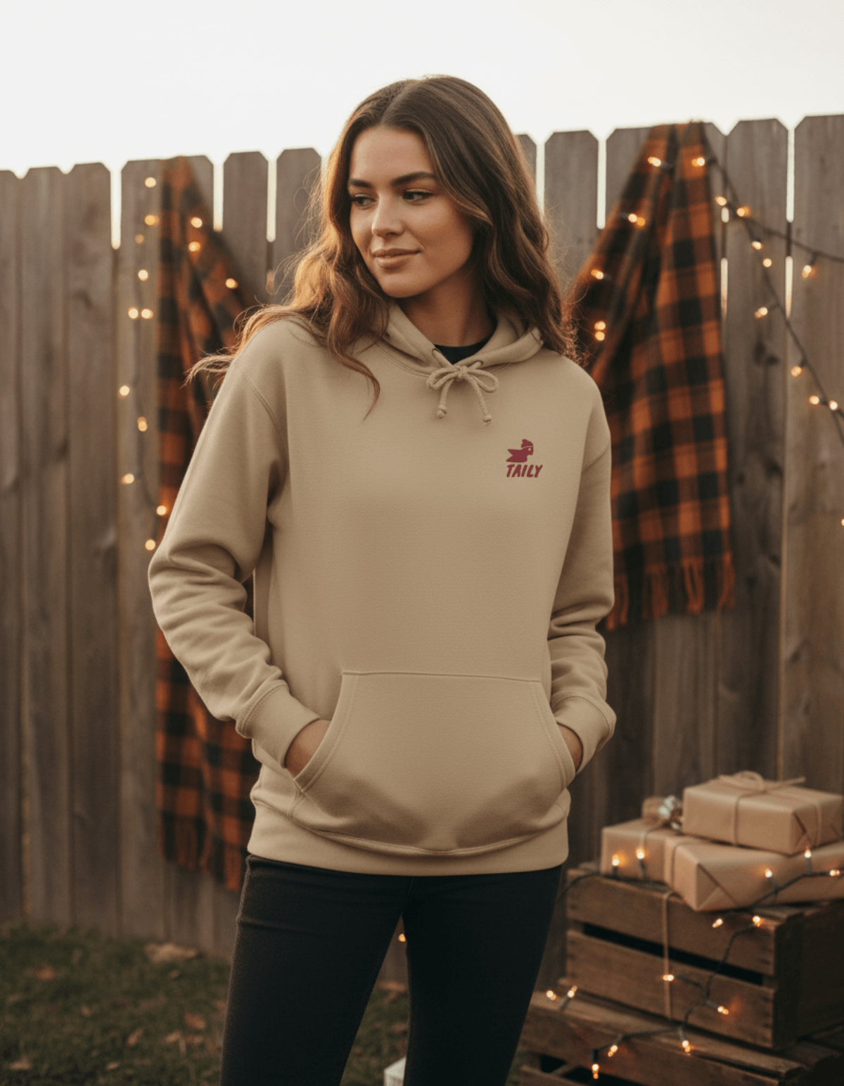 Model wearing Taily Bird Parkland Hoodie – Sandstone in a cozy outdoor setting with festive decor.