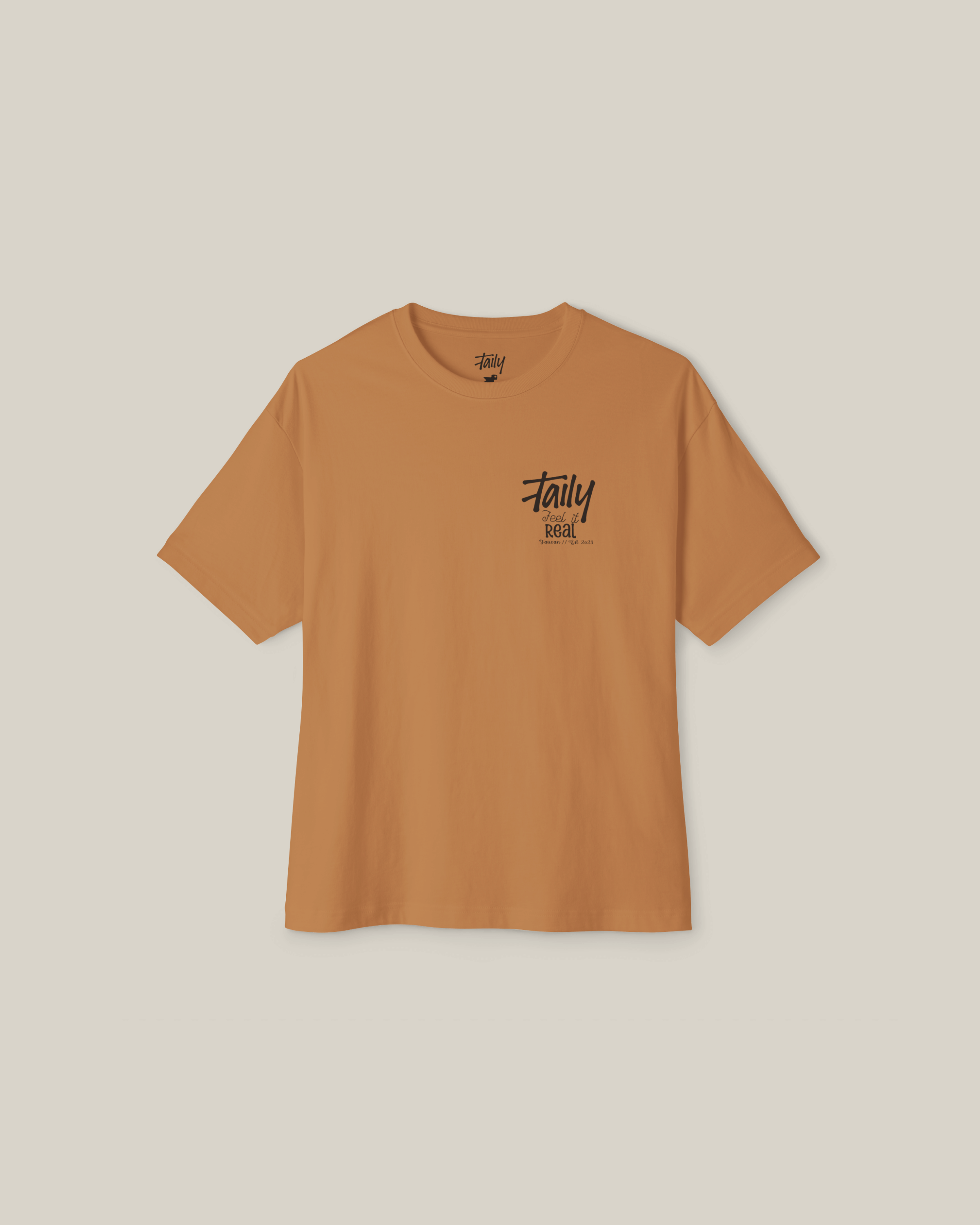 Taily Feel It Real Boxy Tee in toast color with chest logo and bold lettering on the back, representing streetwear style.