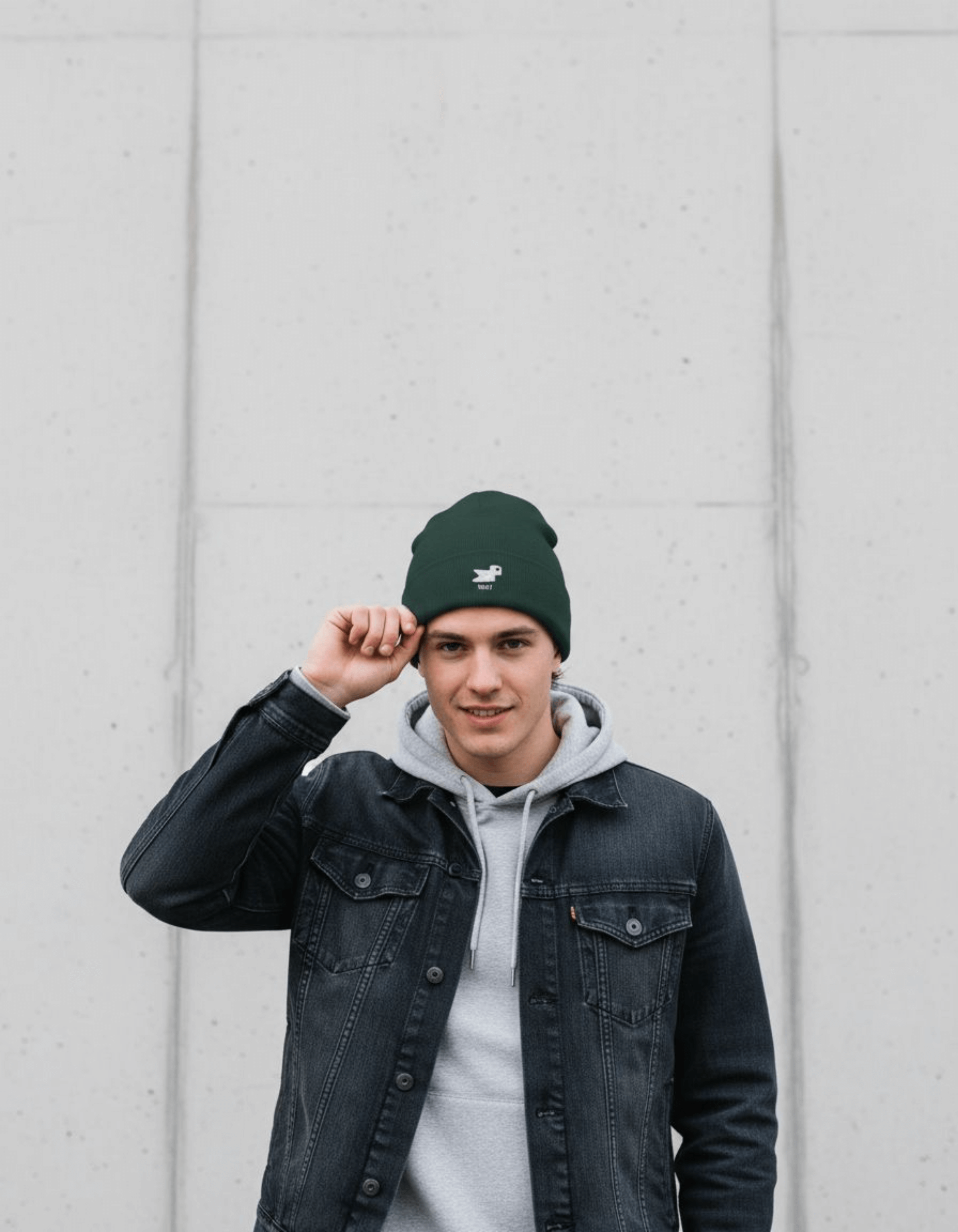 Young man wearing a Taily Bird Knit Beanie in dark green, styled with a denim jacket and hoodie.