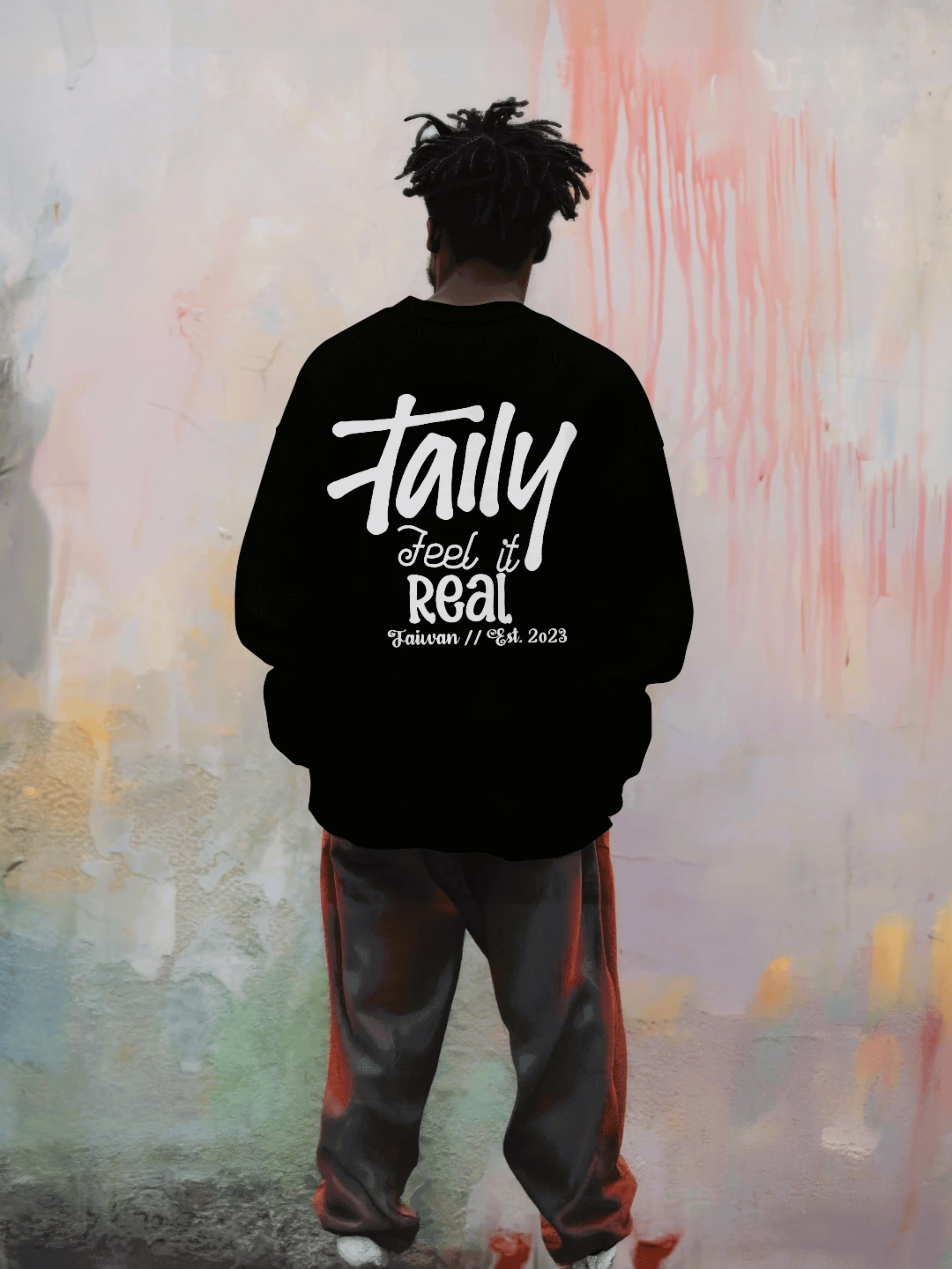 Model wearing black Taily Feel It Real sweatshirt featuring chest logo and bold lettering on the back.