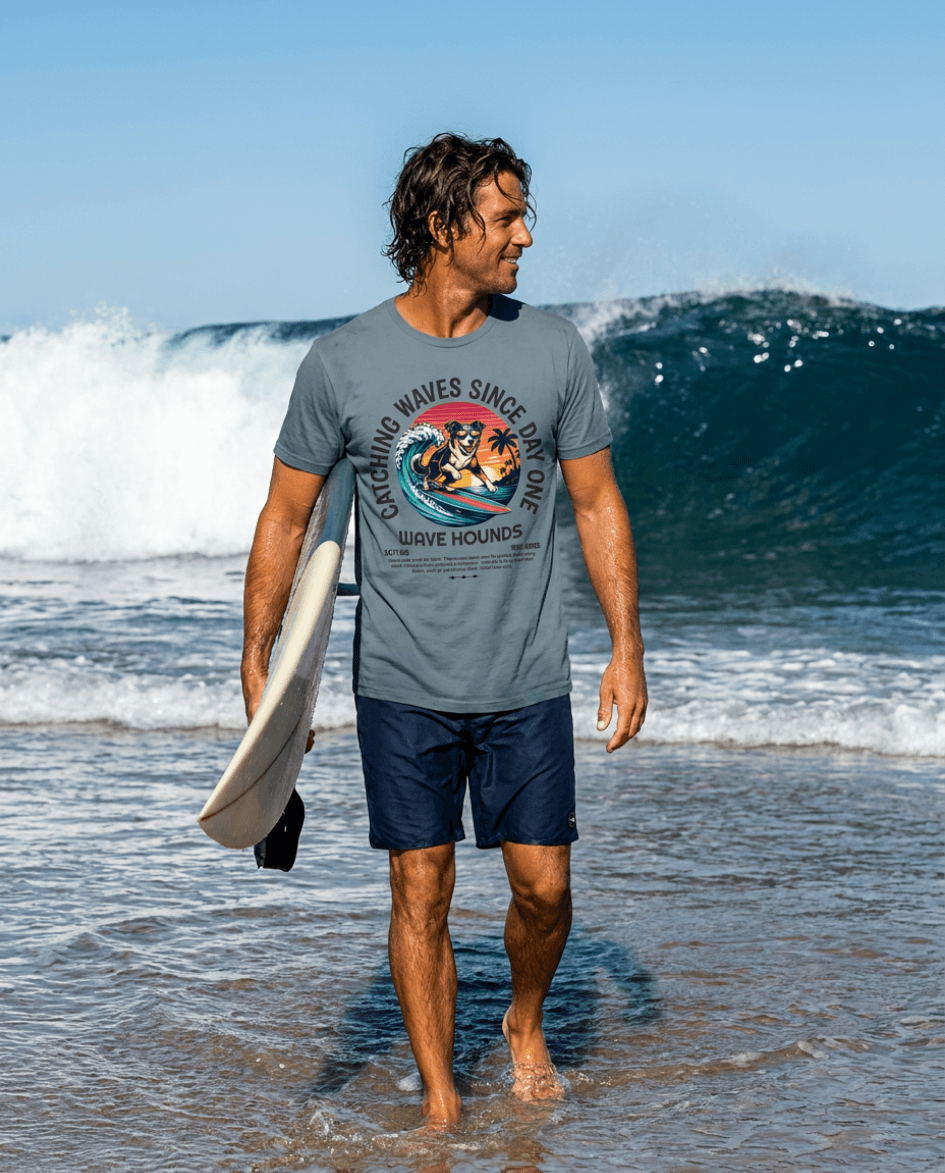 Wave Hounds Surf Tee – Ice Blue on a surfer walking along the beach with a surfboard, waves in the background.