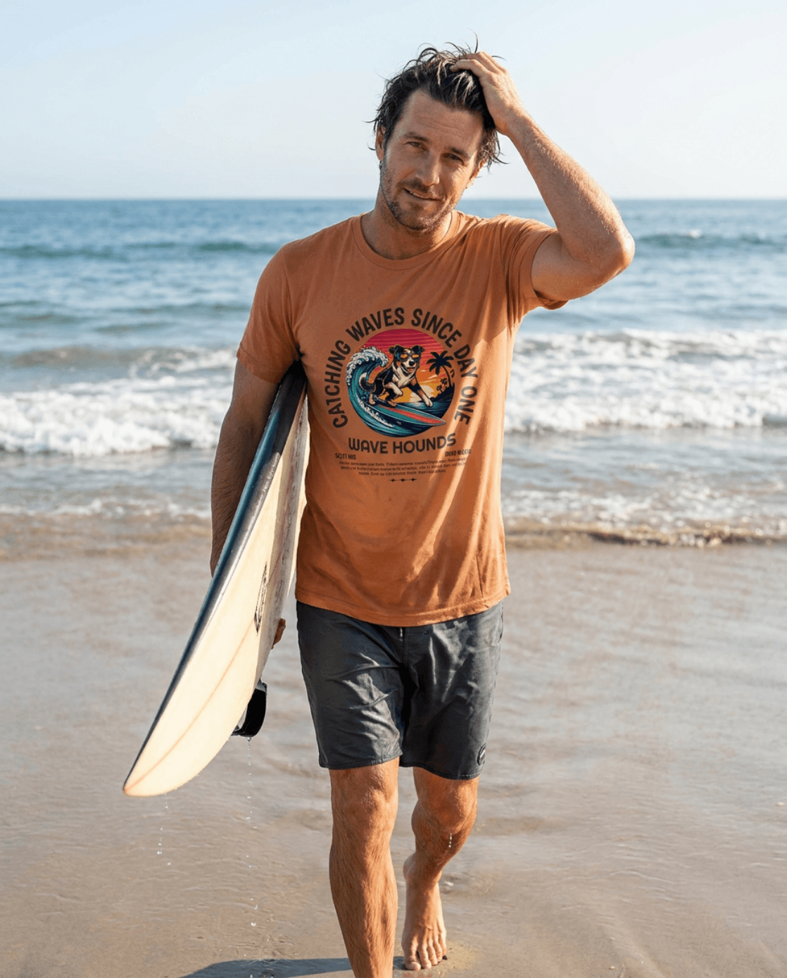 Man wearing Wave Hounds Surf Tee – Yam walking on the beach with a surfboard.