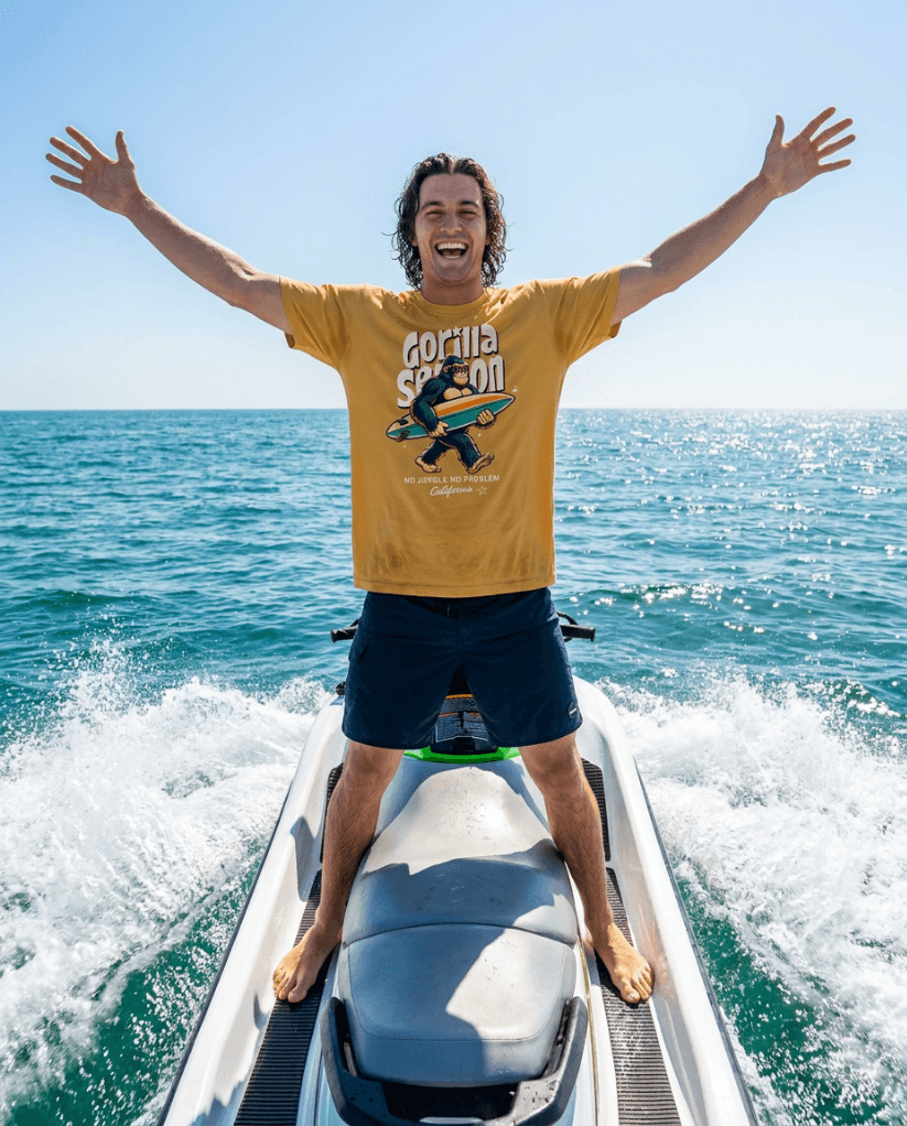 Gorilla Season Surf Tee – Mustard worn by a man on a jet ski, enjoying a sunny beach day.