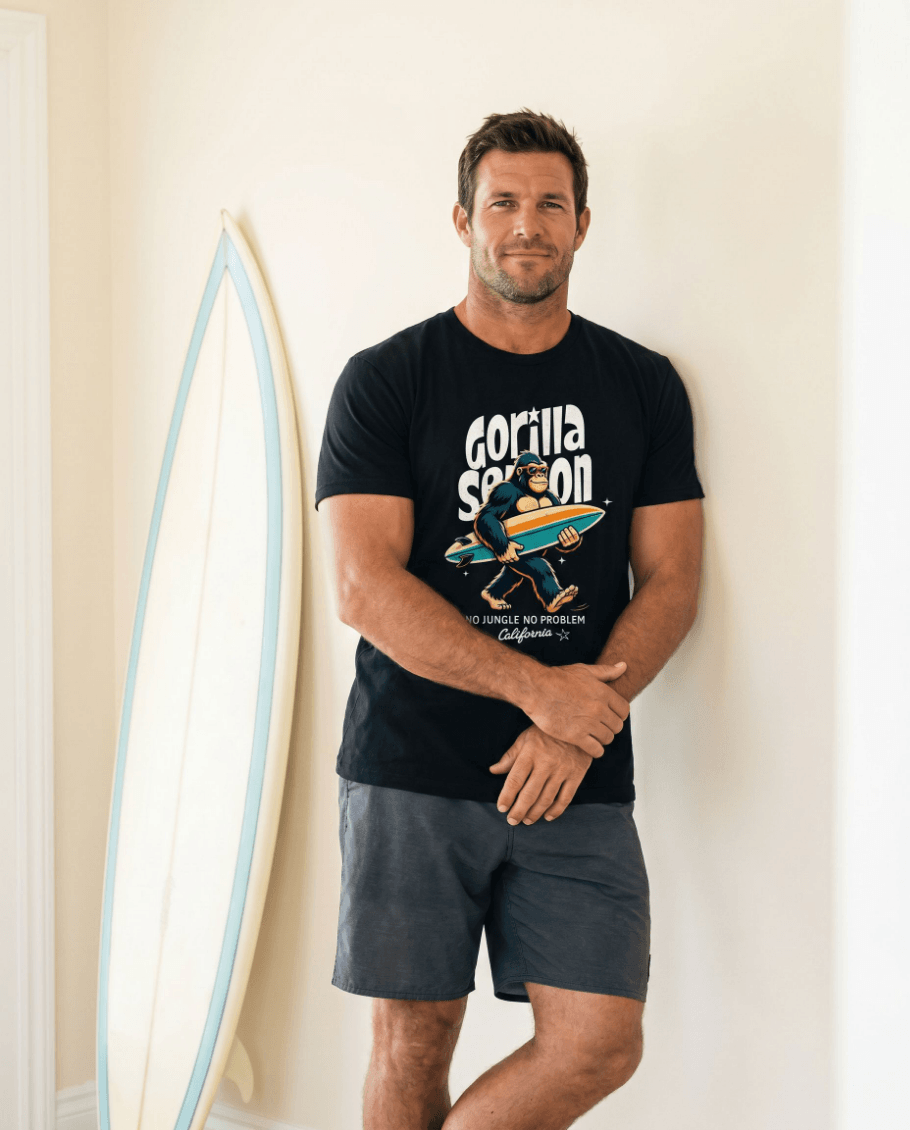 Man wearing Gorilla Season Surf Tee – Black standing next to surfboard, showcasing California surf graphic.