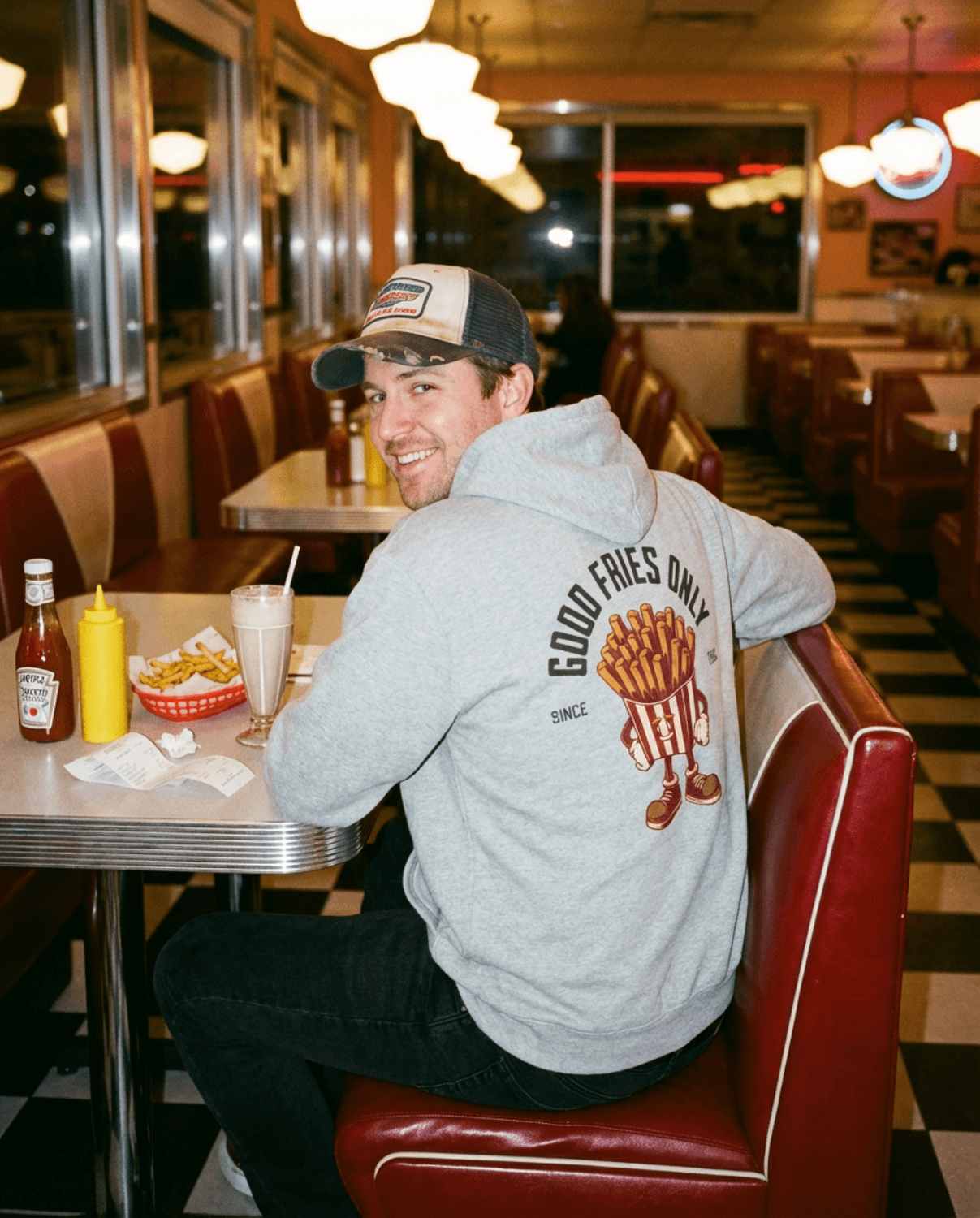 Man wearing Good Fries Only Retro French Fries Hoodie – Sport Grey in a diner, enjoying fries and a milkshake.