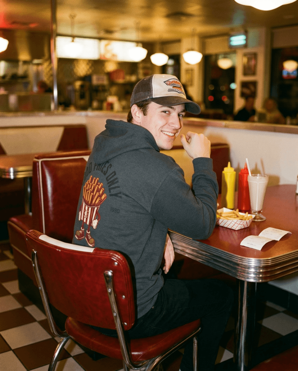 Good Fries Only Retro French Fries Hoodie – Dark Heather worn in a vintage diner setting with ketchup and mustard.