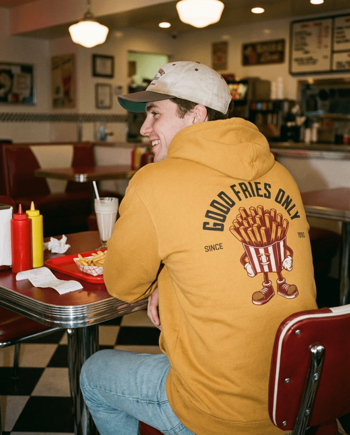 Good Fries Only Retro French Fries Hoodie – Mustard worn in a nostalgic diner setting with classic fast food decor.