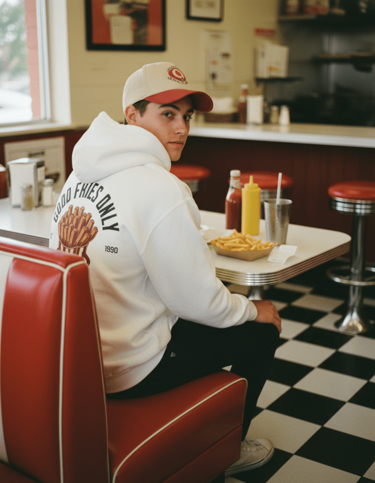 Good Fries Only Retro French Fries Hoodie – White worn by a young man in a diner with fries and condiments.
