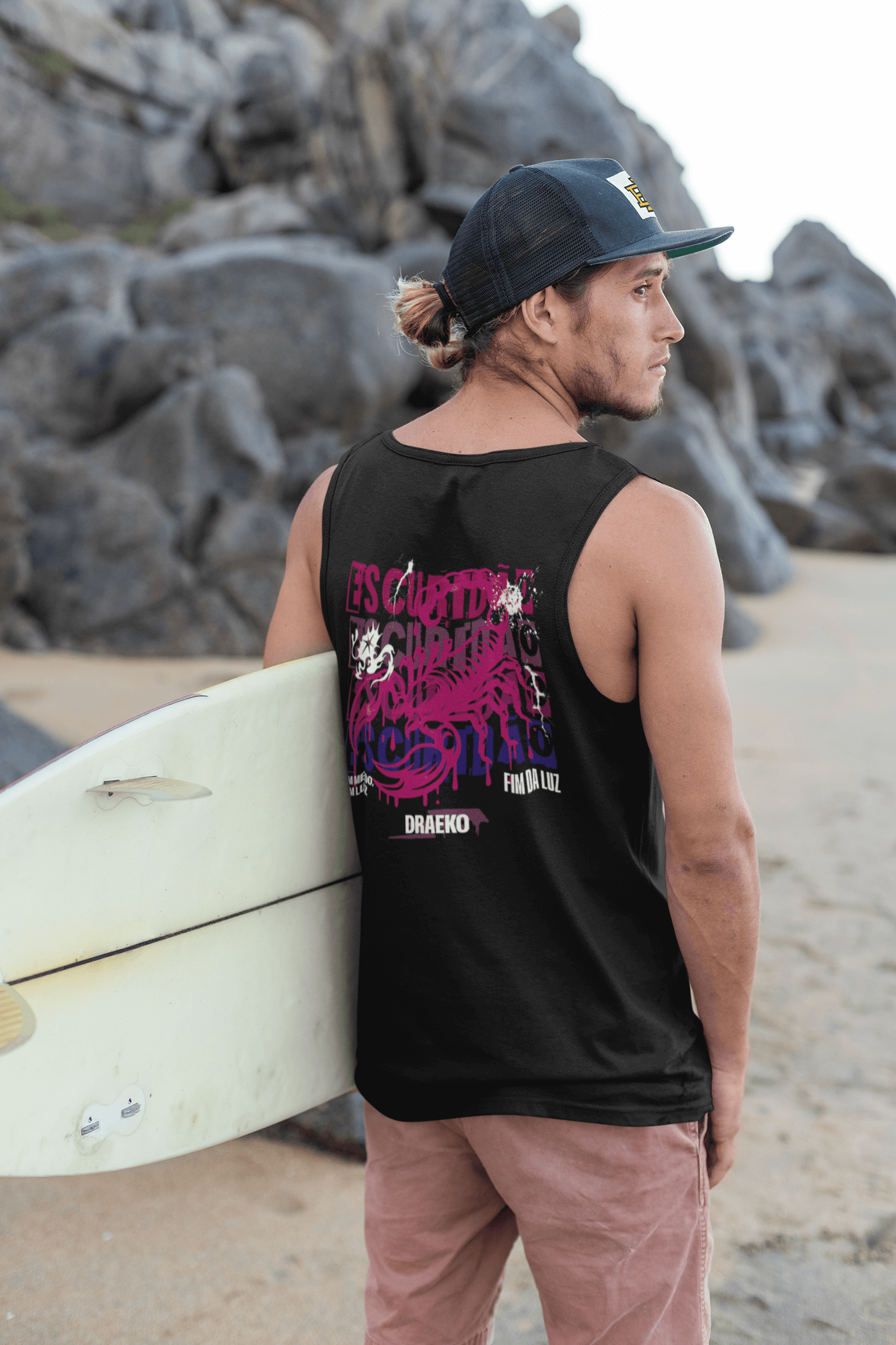 Male model wearing Taily Scorpion Graphic Tank Top with surfboard on beach, showcasing black and pink graphic design.