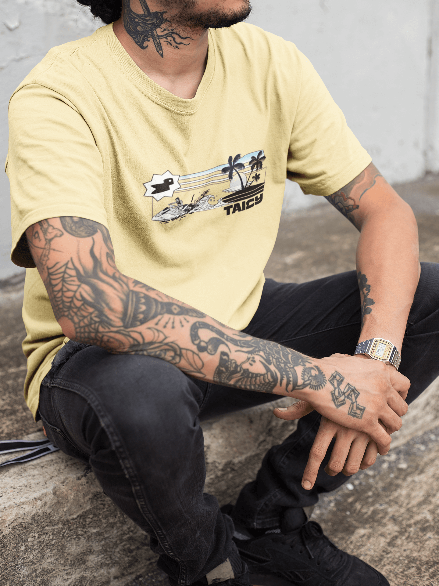Taily Summer Souvenir Tee featuring jet ski splash, palm lines, and bold logo, worn by a tattooed man.