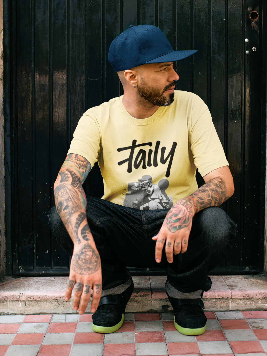 Man wearing Taily Street Rebel graphic tee in butter color, showcasing streetwear style with tattoos and casual pose.