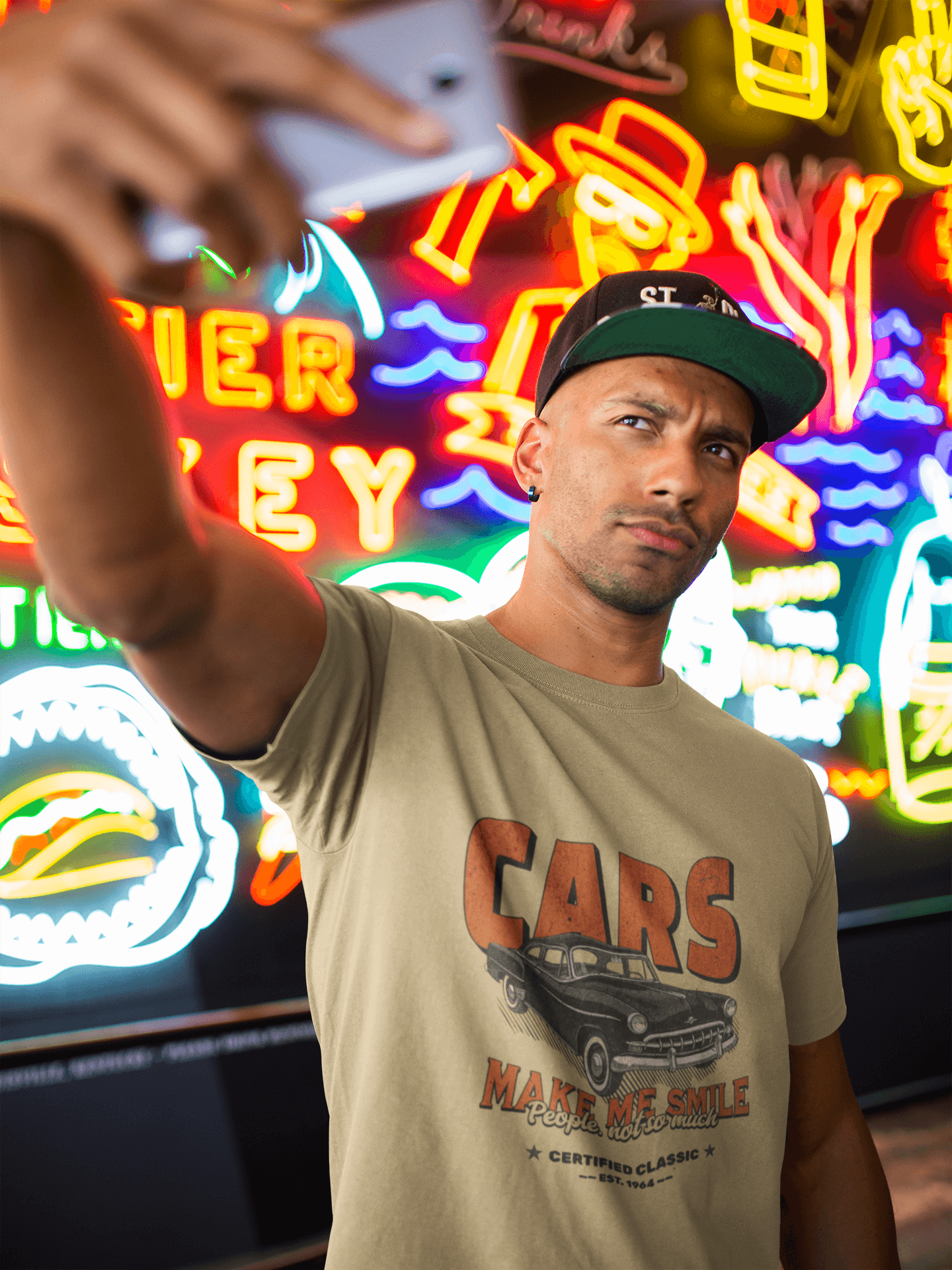Man wearing Unisex Classic Car T-Shirt, smiling near colorful neon signs, showcasing vintage car nostalgia.