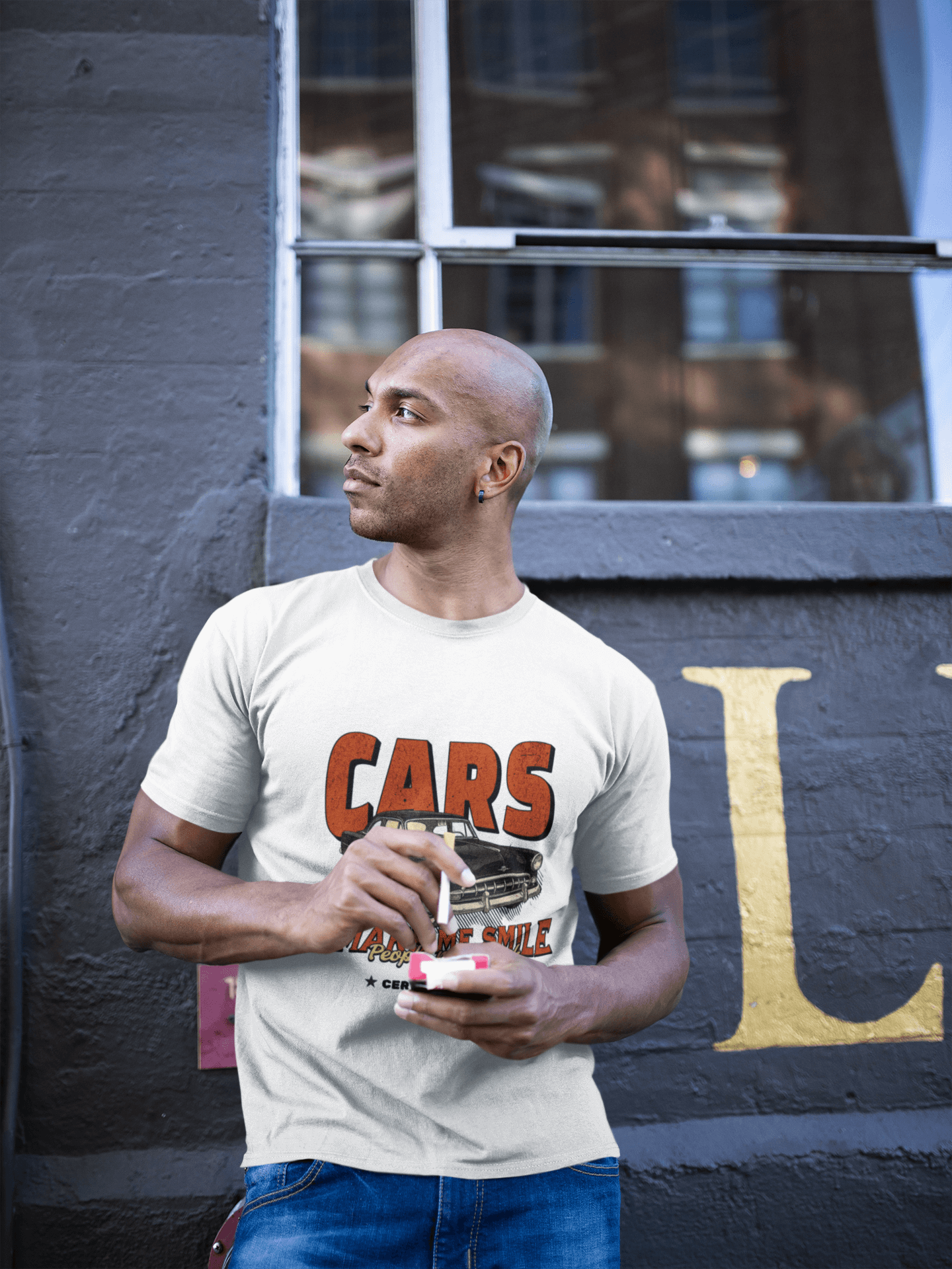 Man wearing Unisex Classic Car T-Shirt with 'Cars Make Me Smile' design, standing against urban backdrop.