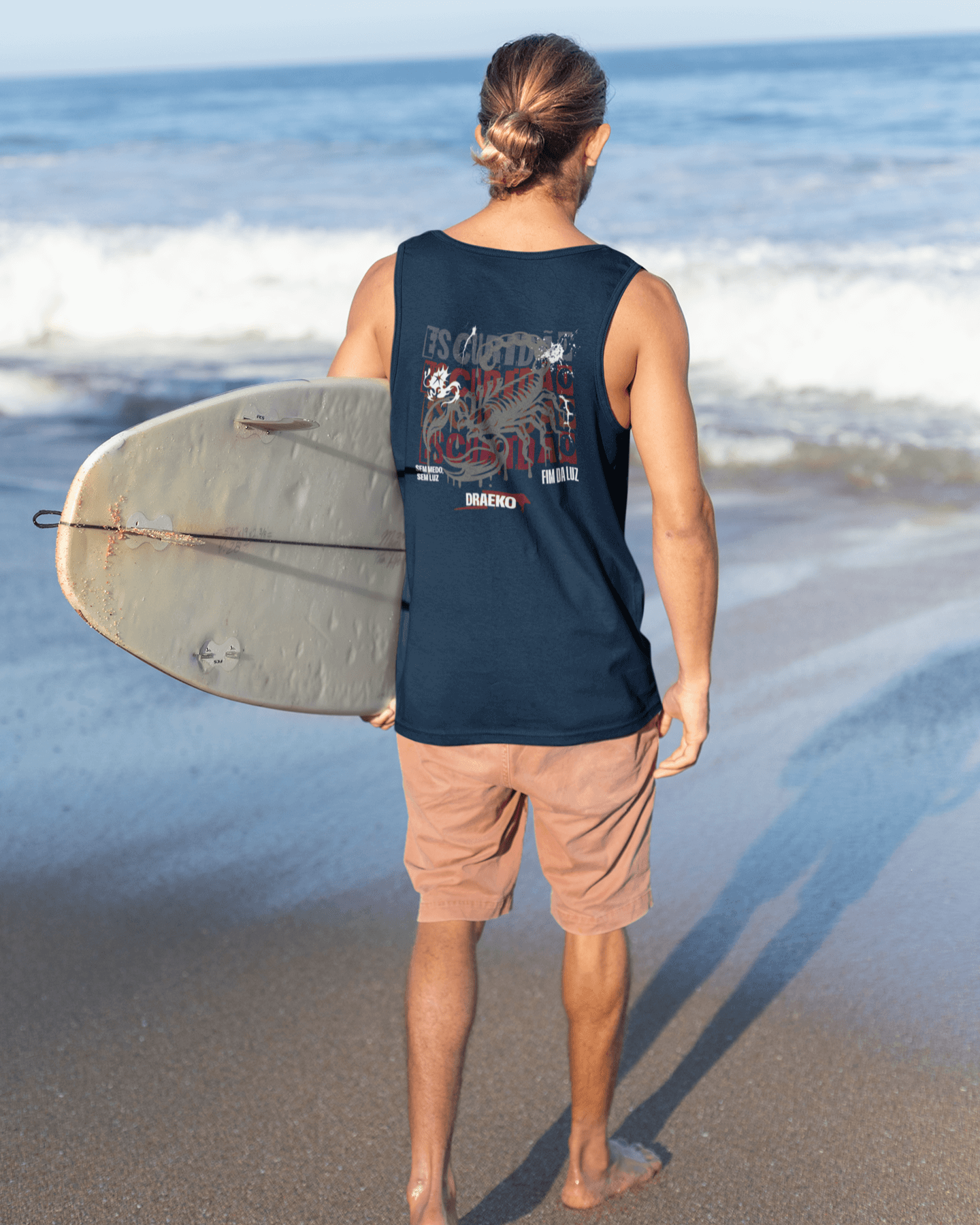 Man wearing Taily Scorpion graphic tank in navy, holding surfboard at beach, showcasing bold red scorpion design.