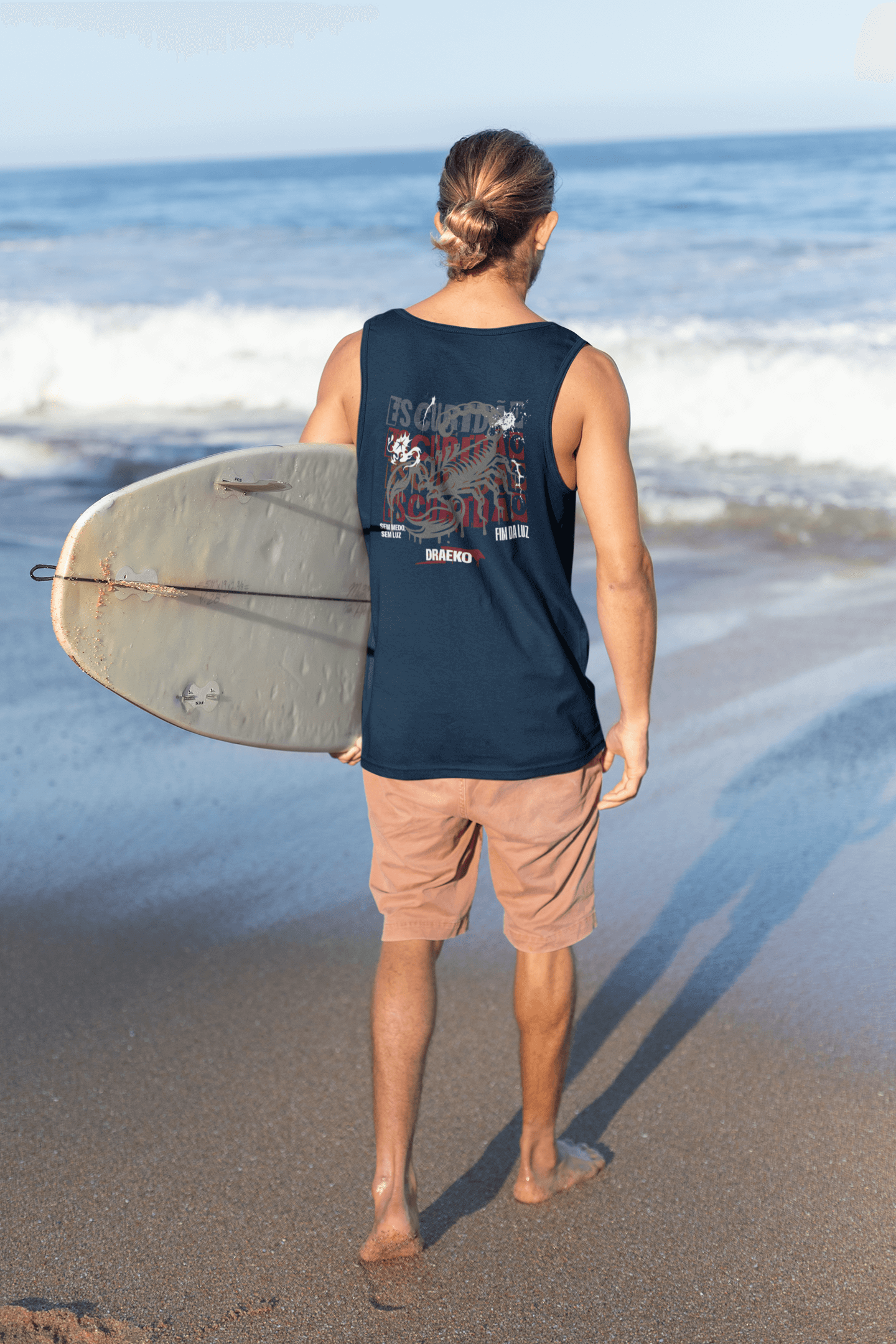 Man wearing Taily Scorpion Graphic Tank while holding a surfboard on the beach, showcasing a navy red print.
