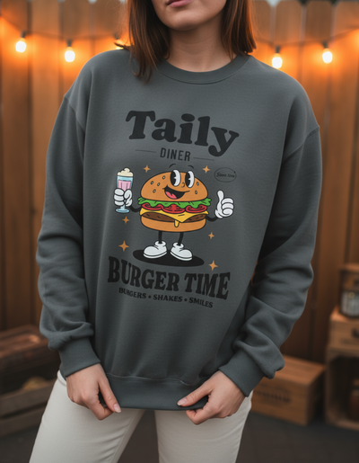 Model wearing Taily Diner Burger Time sweatshirt in pepper color featuring a cheerful burger mascot and slogan.