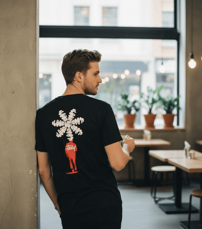 Man wearing Taily Bloom streetwear graphic t-shirt in black with bold back design in urban cafe setting.