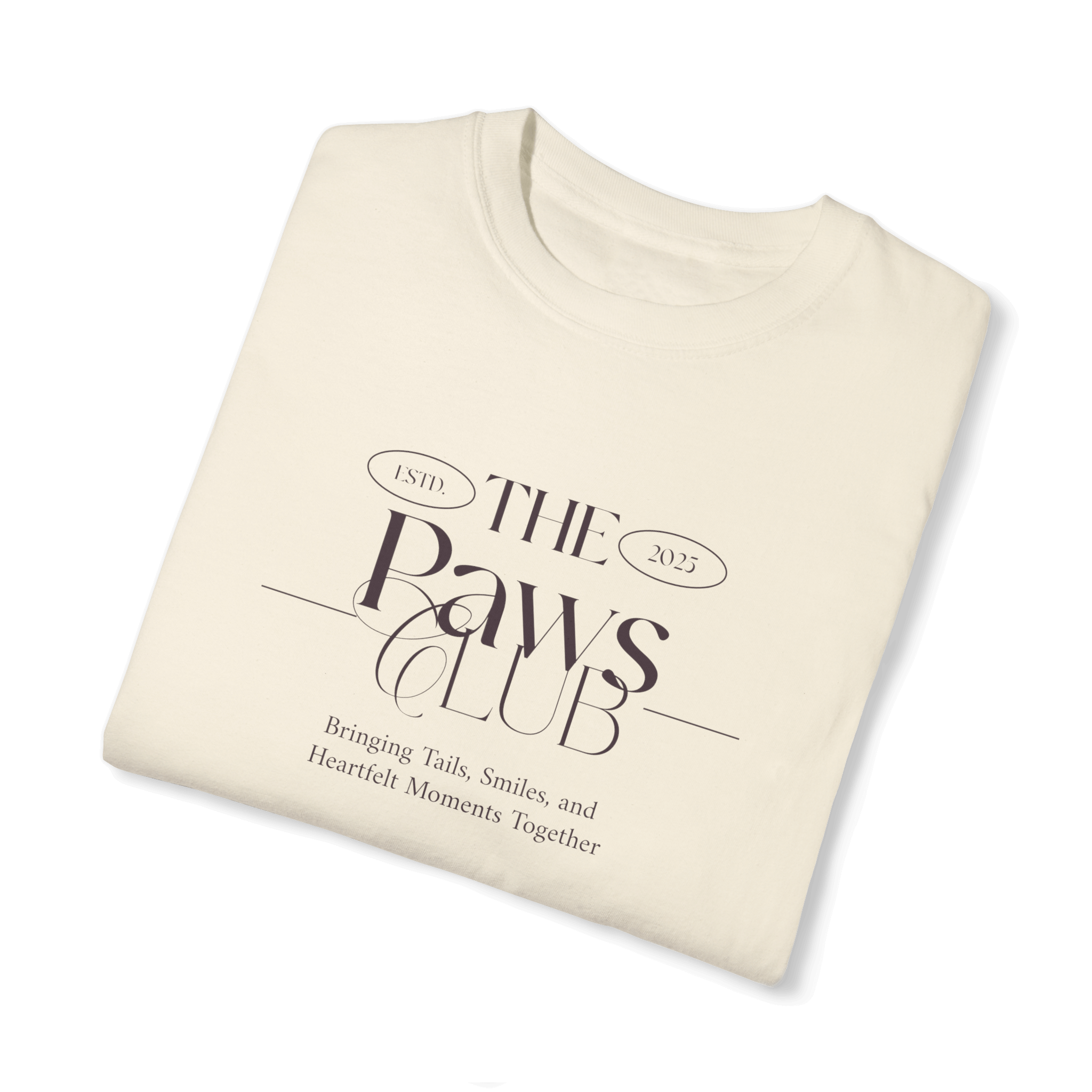 Folded beige T-shirt featuring 'The Paws Club' logo in elegant typography with the tagline 'Bringing Tails, Smiles, and Heartfelt Moments Together,' highlighting a minimalist and sophisticated design.