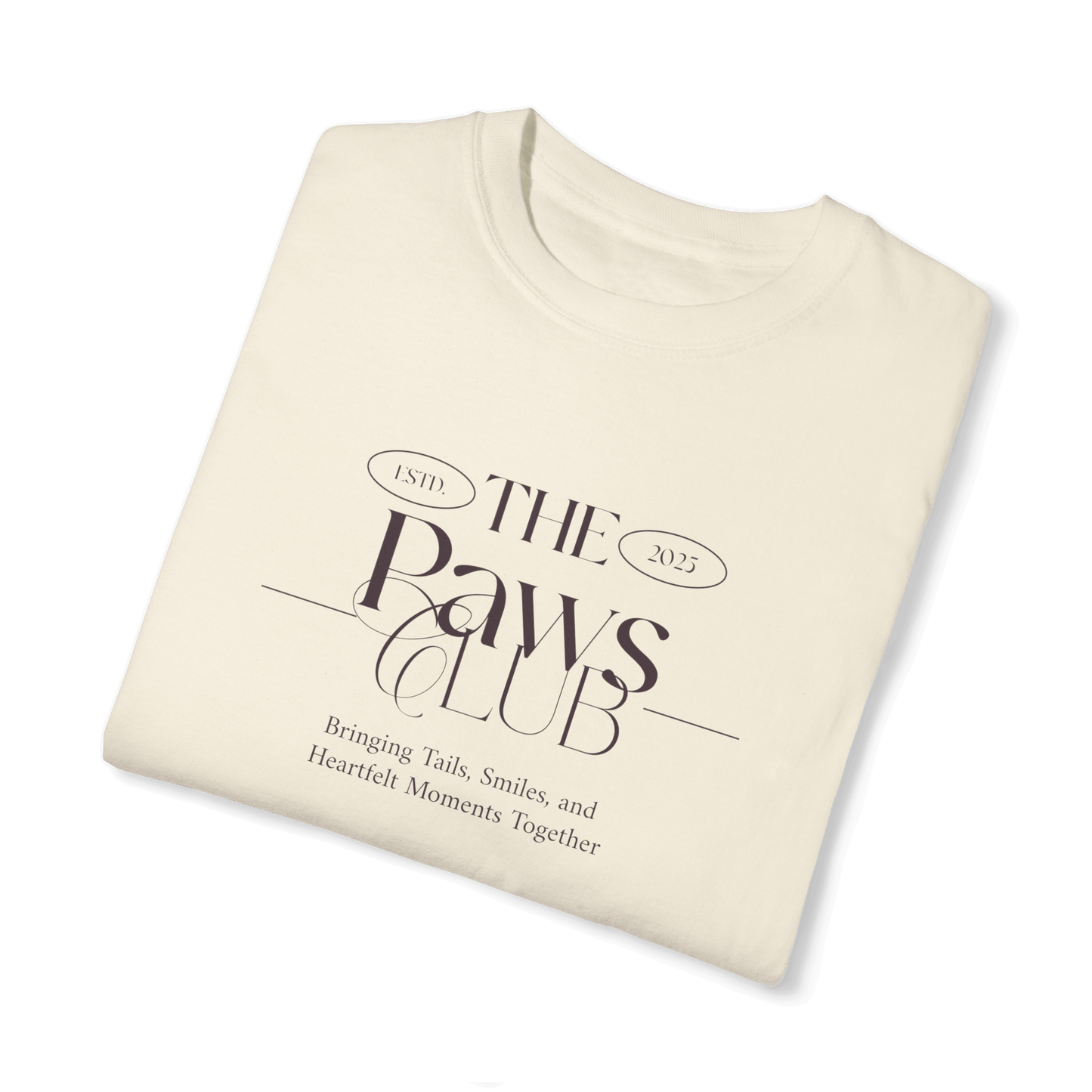 Folded beige T-shirt featuring 'The Paws Club' logo in elegant typography with the tagline 'Bringing Tails, Smiles, and Heartfelt Moments Together,' highlighting a minimalist and sophisticated design.