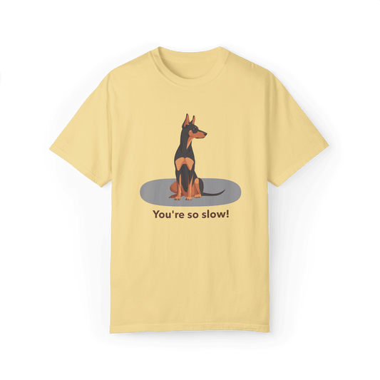 A pale yellow T-shirt featuring a cartoon Doberman illustration with the humorous text "You're so slow!" showcasing a playful and relaxed vibe.