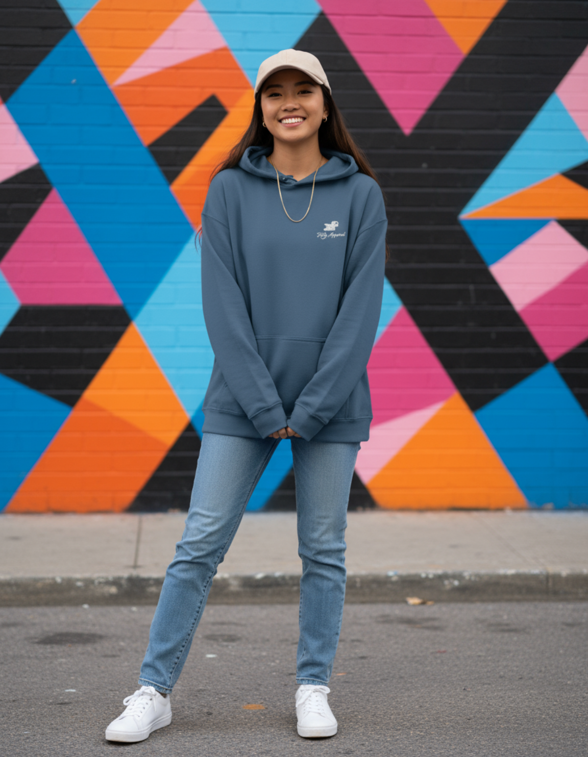 Model wearing Taily Bird embroidered hoodie in indigo blue against a colorful geometric mural.