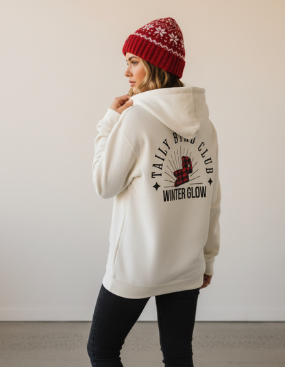 Woman wearing Taily Bird Club Winter Glow Hoodie in bone color, showcasing the back graphic and red knit hat.