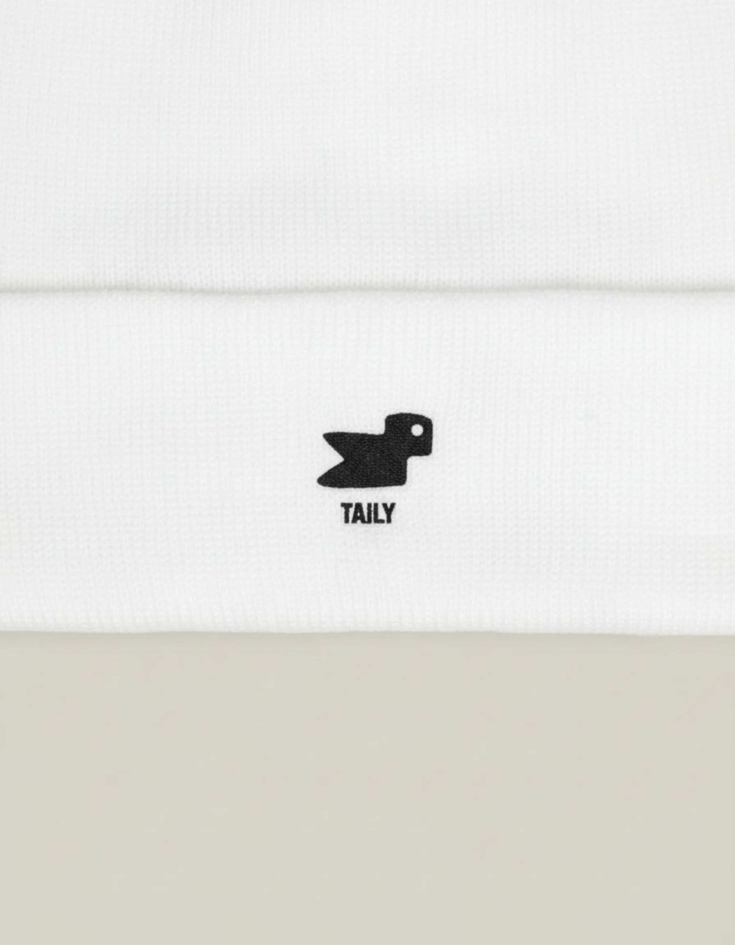 Taily Bird Knit Beanie showing minimal black embroidery on a white fabric, emphasizing comfort and streetwear style.