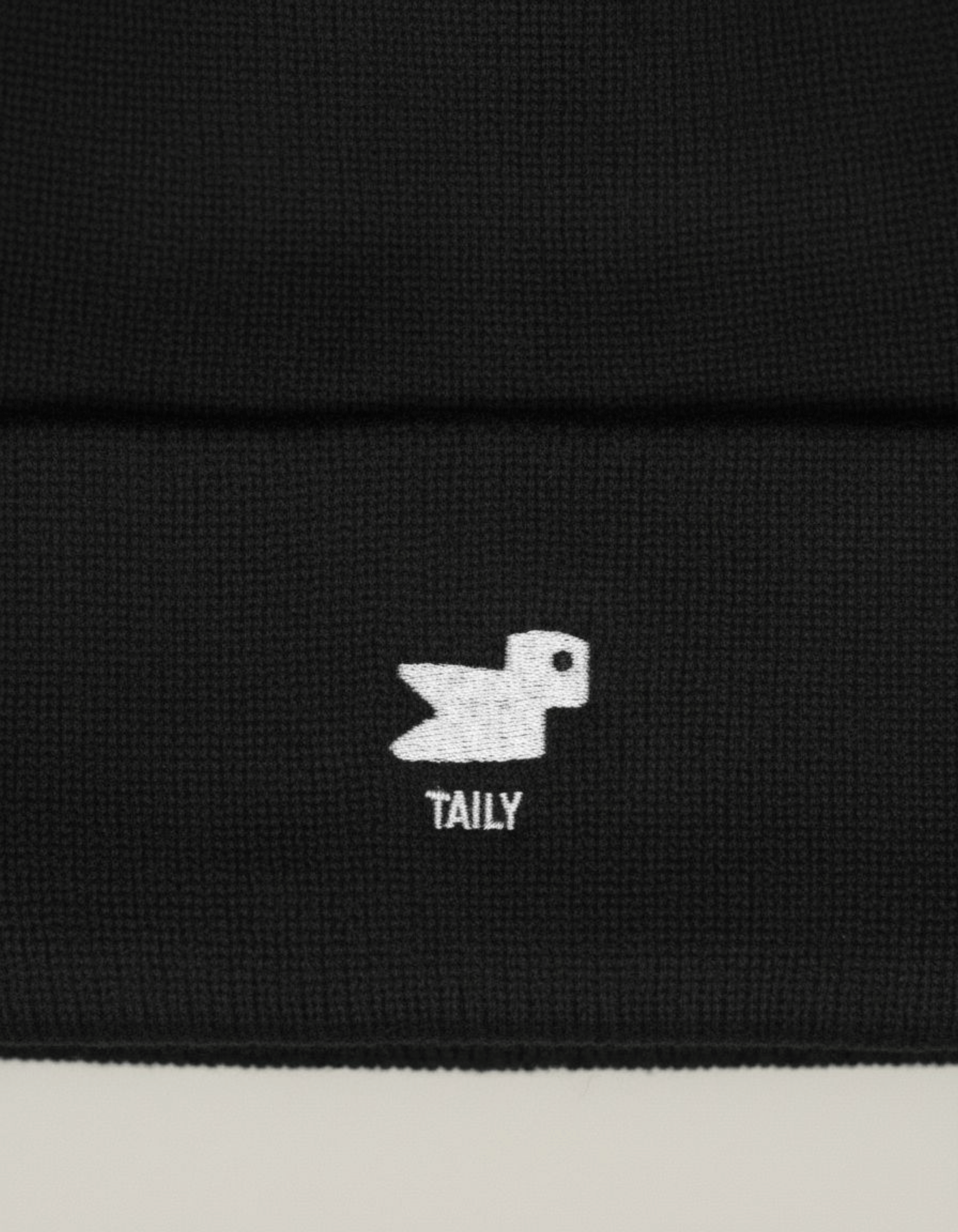 Taily Bird Knit Beanie – Black close-up showing the minimal embroidery detail of the logo.