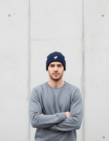 Man in a gray sweater wearing a Taily Bird Knit Beanie in dark navy against a concrete wall.