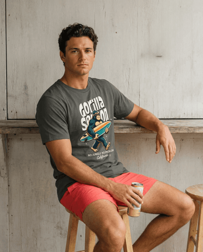 Gorilla Season Surf Tee – Pepper displayed by a model sitting on a stool, showcasing a laid-back style.