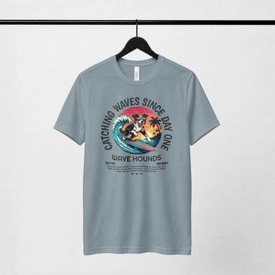 Wave Hounds Surf Tee – Ice Blue displayed on hanger with vibrant surf graphic and retro styling.