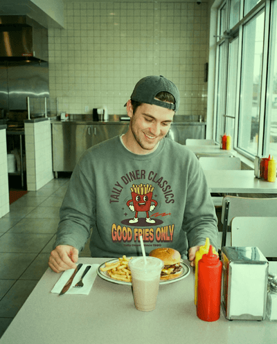 Good Fries Only Sweatshirt – Taily Diner (Grey) worn by a man at a diner table with food.