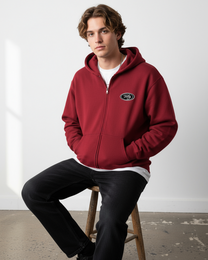 Taily Zip Hoodie – Classic Embroidered Streetwear in Cardinal Red, model wearing hoodie sitting on a stool.