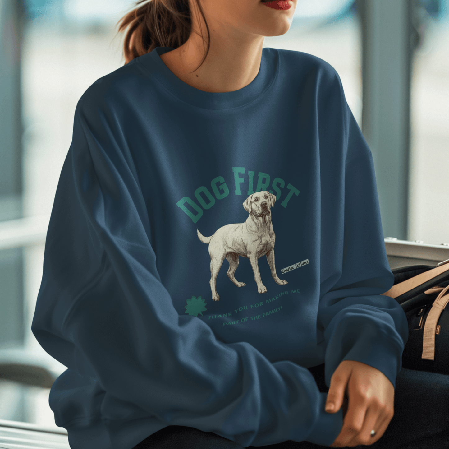 Female model wearing a navy blue "Dog First" illustration sweatshirt featuring a Labrador design, set against an airport waiting area background.