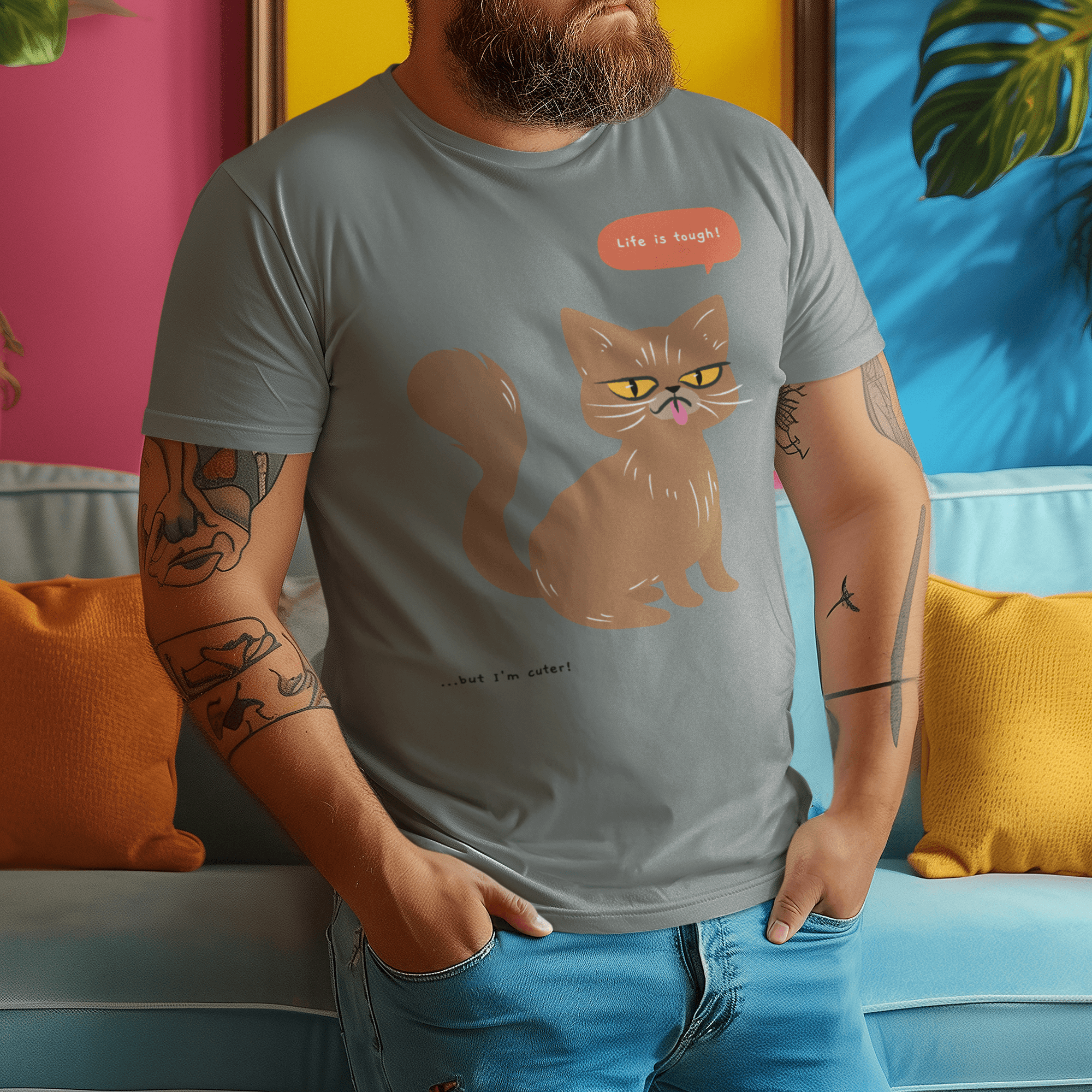 Bearded man wearing a gray T-shirt with a humorous cat design, standing against a colorful background.