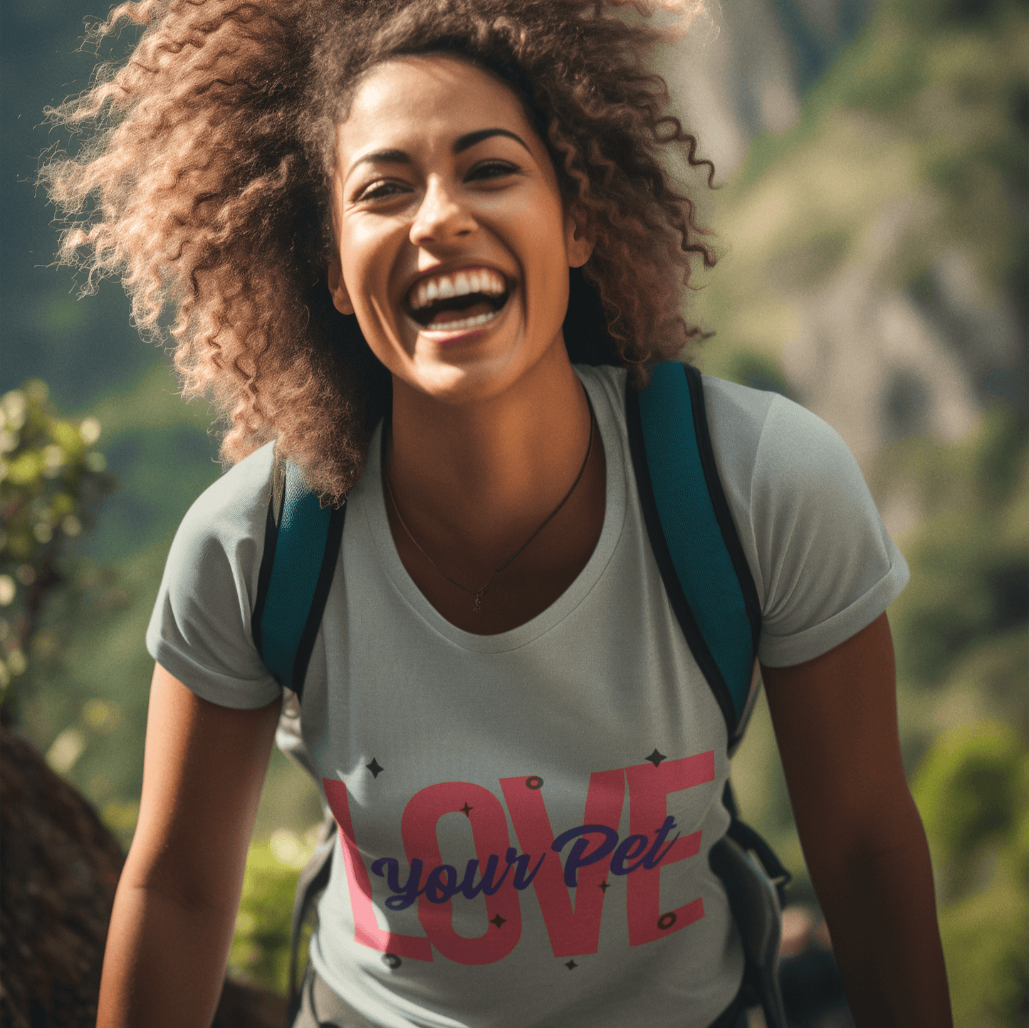 Smiling woman wearing a light gray T-shirt with a bold 'Love Your Pet' design in pink and blue, enjoying a hike in a scenic mountainous area.