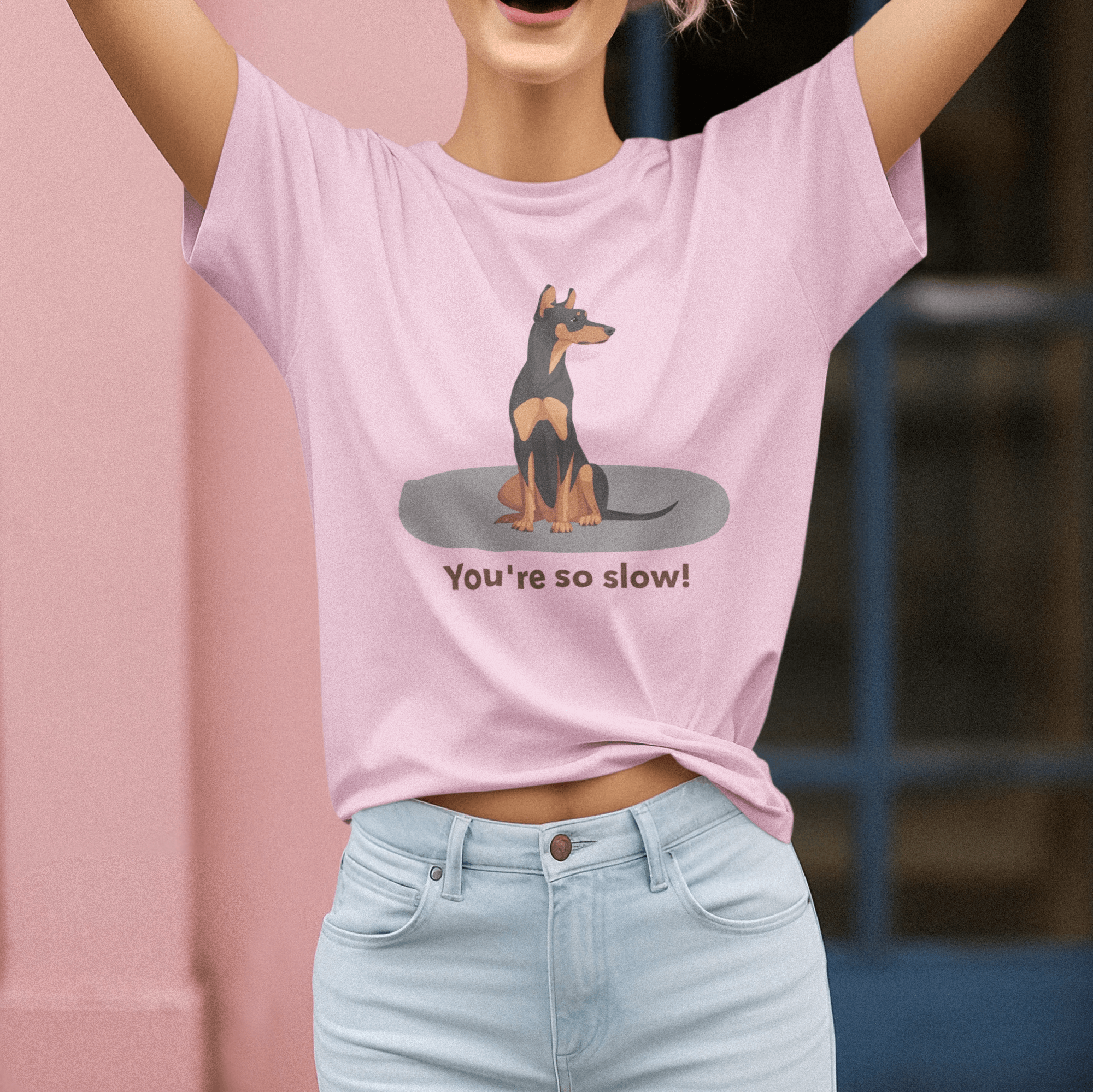 A cheerful woman wearing a pink T-shirt featuring a cartoon Doberman illustration with the humorous text 