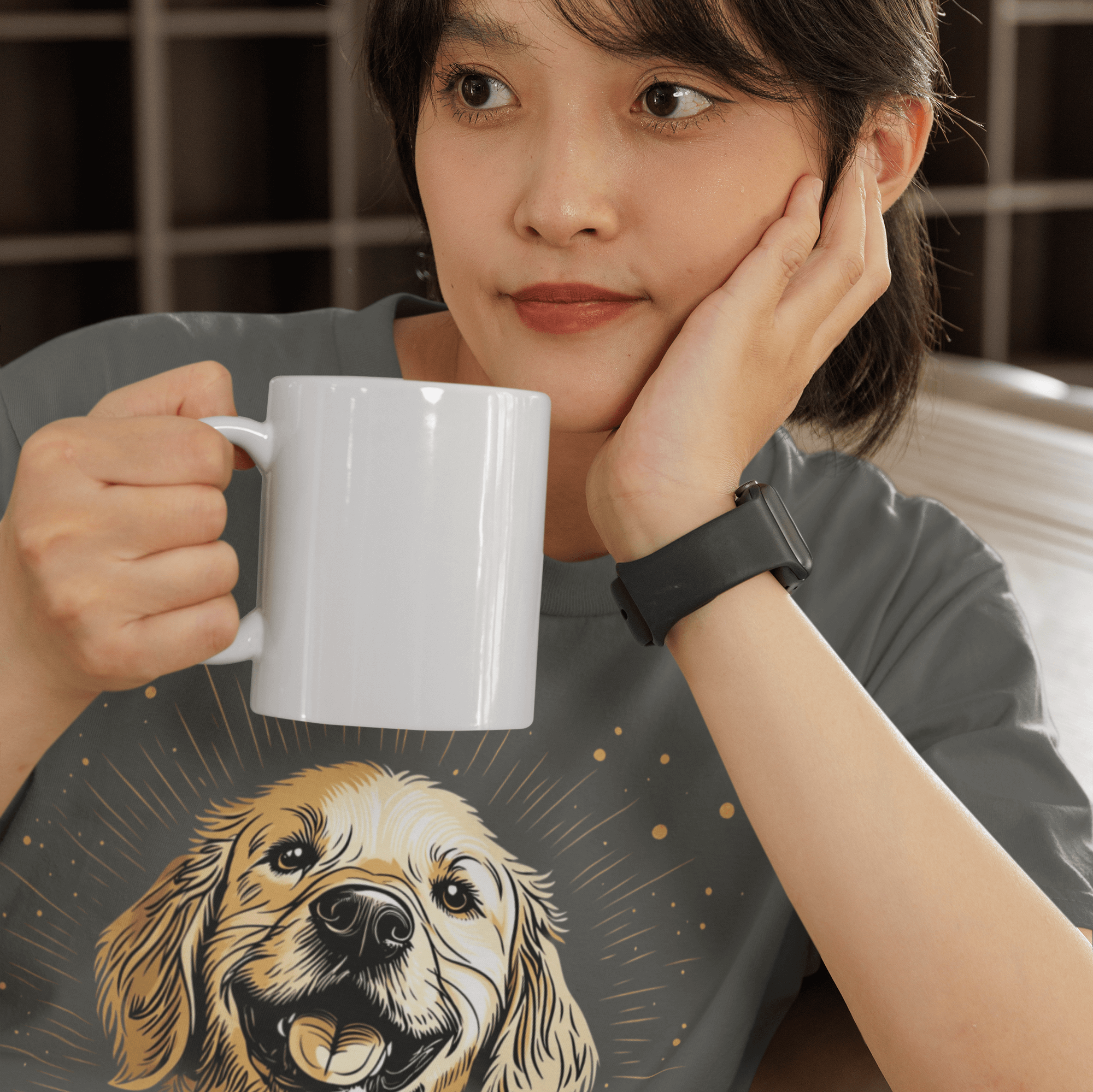 Woman resting her head on her hand, holding a white coffee mug, wearing a dark gray T-shirt featuring a smiling Golden Retriever illustration and the text 