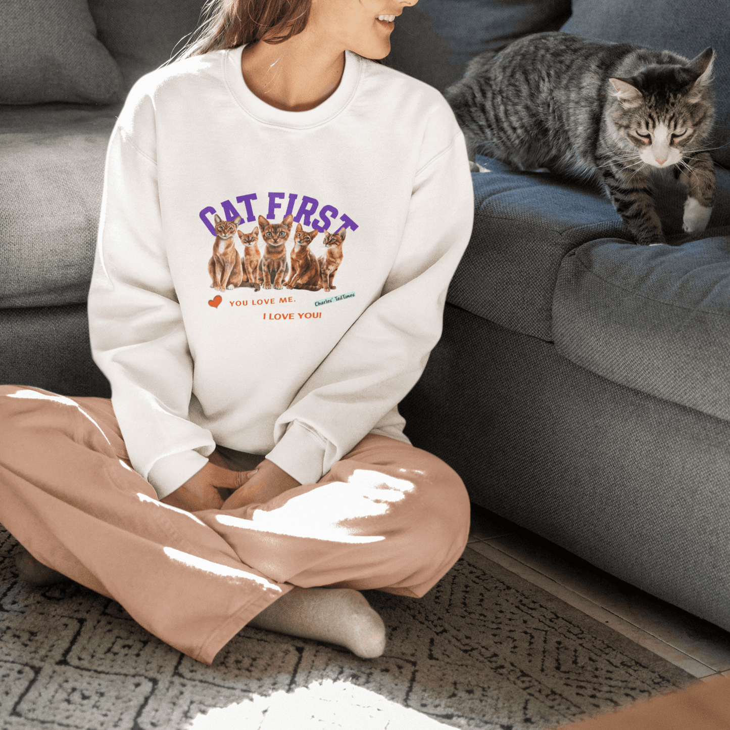 White sweatshirt featuring a graphic of four Abyssinian cats in brown with the text 'Cat First' in purple, accompanied by the phrases 'You love me. I love you!' in red, with a heart icon and branding from Charles TailTimes.