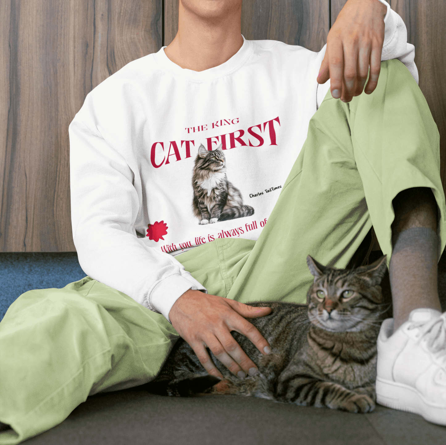 White sweatshirt featuring a Maine Coon cat graphic with the text "The King CAT FIRST" in red. A smiling man sits with his tabby cat.