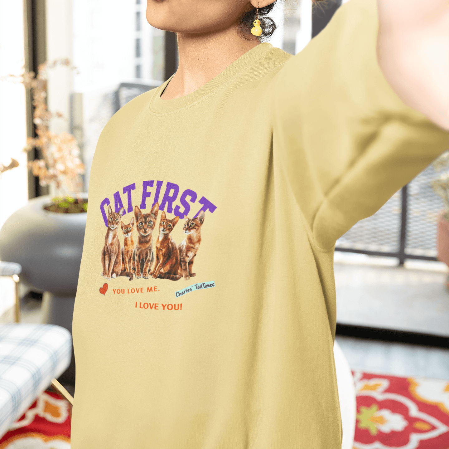 Woman wearing a yellow sweatshirt featuring Abyssinian cats and the text "Cat First," with the red phrases "You love me. I love you!" posing for a selfie with a kiss face.