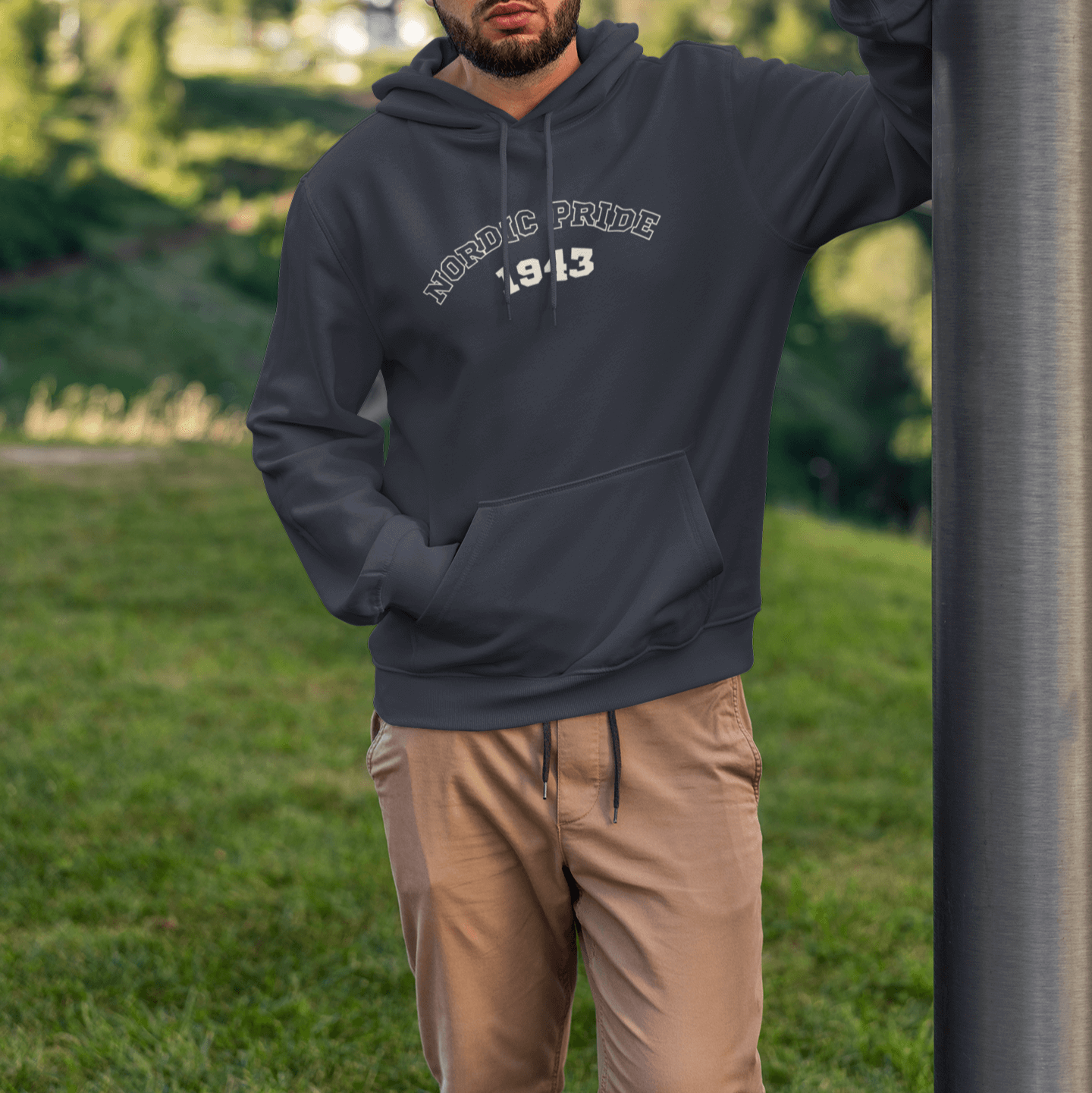 Man wearing a relaxed fit Swedish Vallhund hoodie with "NORDIC PRIDE 1943" design, set in a green outdoor environment.