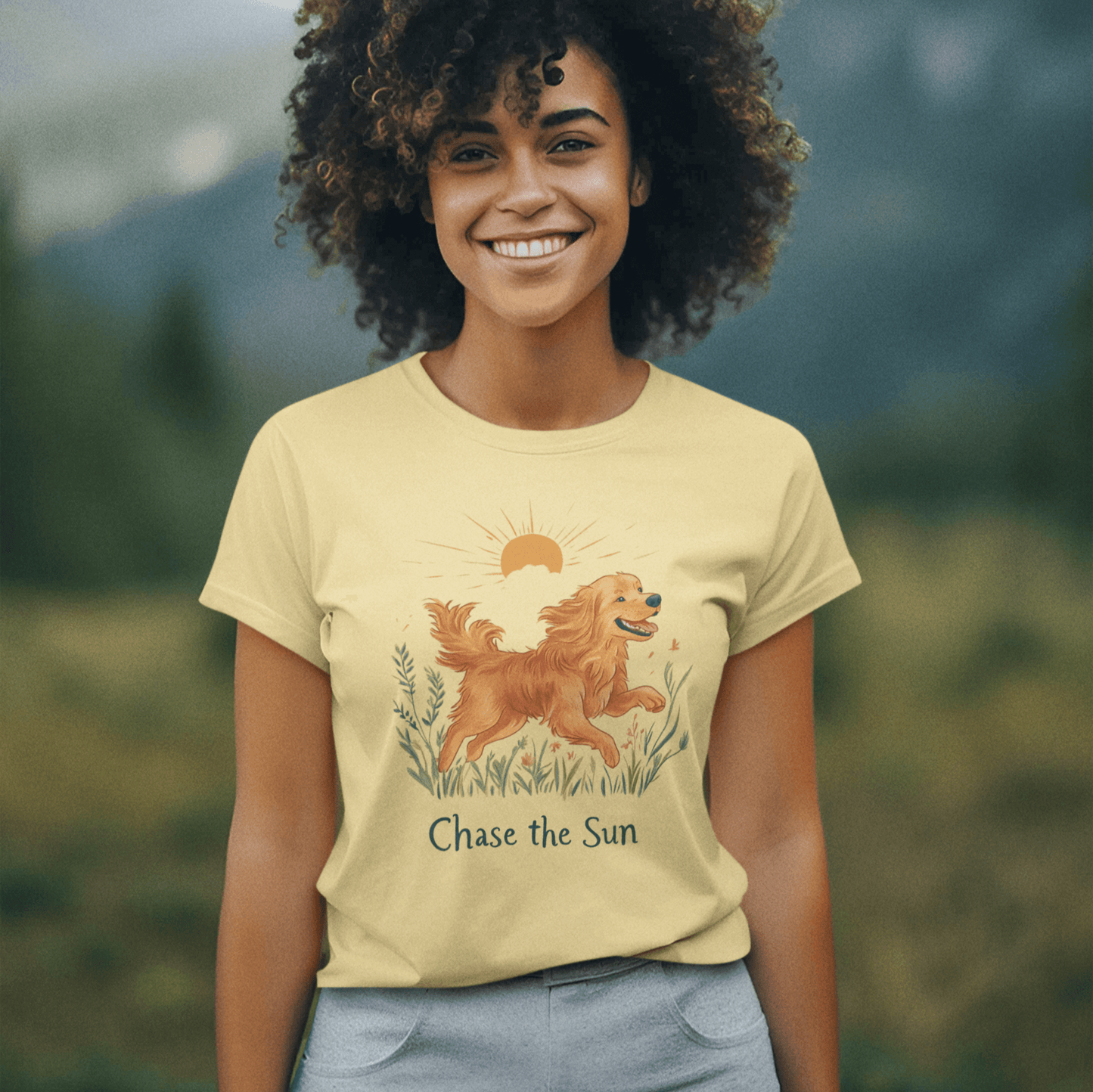 A woman wearing a "Chase the Sun" golden retriever illustration T-shirt, set against a scenic mountain background, showcasing a lively and natural vibe.