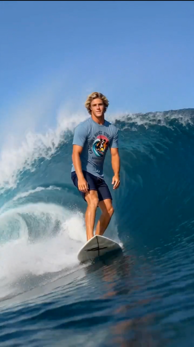 Surfer wearing Wave Hounds Surf Tee – Ice Blue riding a wave under sunny skies.