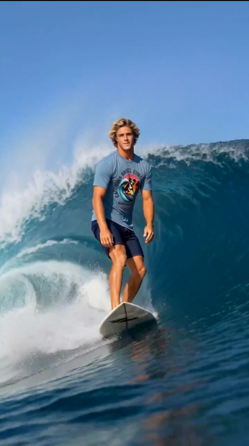 Wave Hounds Surf Tee – White worn by a surfer riding a wave, showcasing the bold retro graphic design.