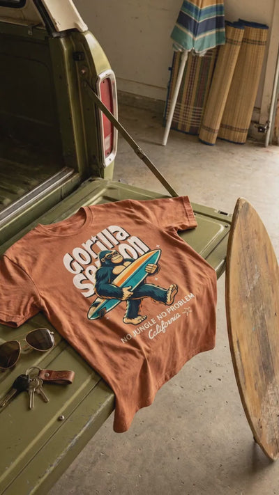 Gorilla Season Surf Tee – Yam displayed on a vintage truck, showcasing its bold surf graphic and burnt orange color.